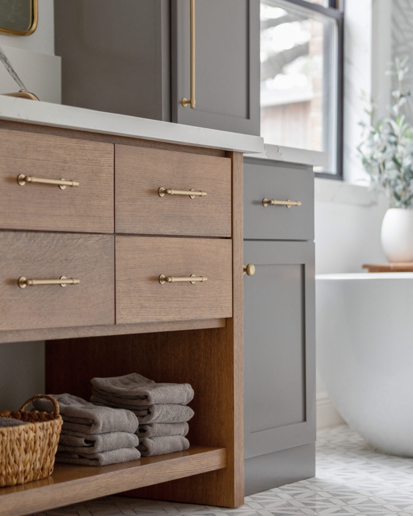 White oak drawer bank with brass pulls above an open shelf of folded towels in the Evergreen Suite Bathroom project by Jennifer Kizzee Design