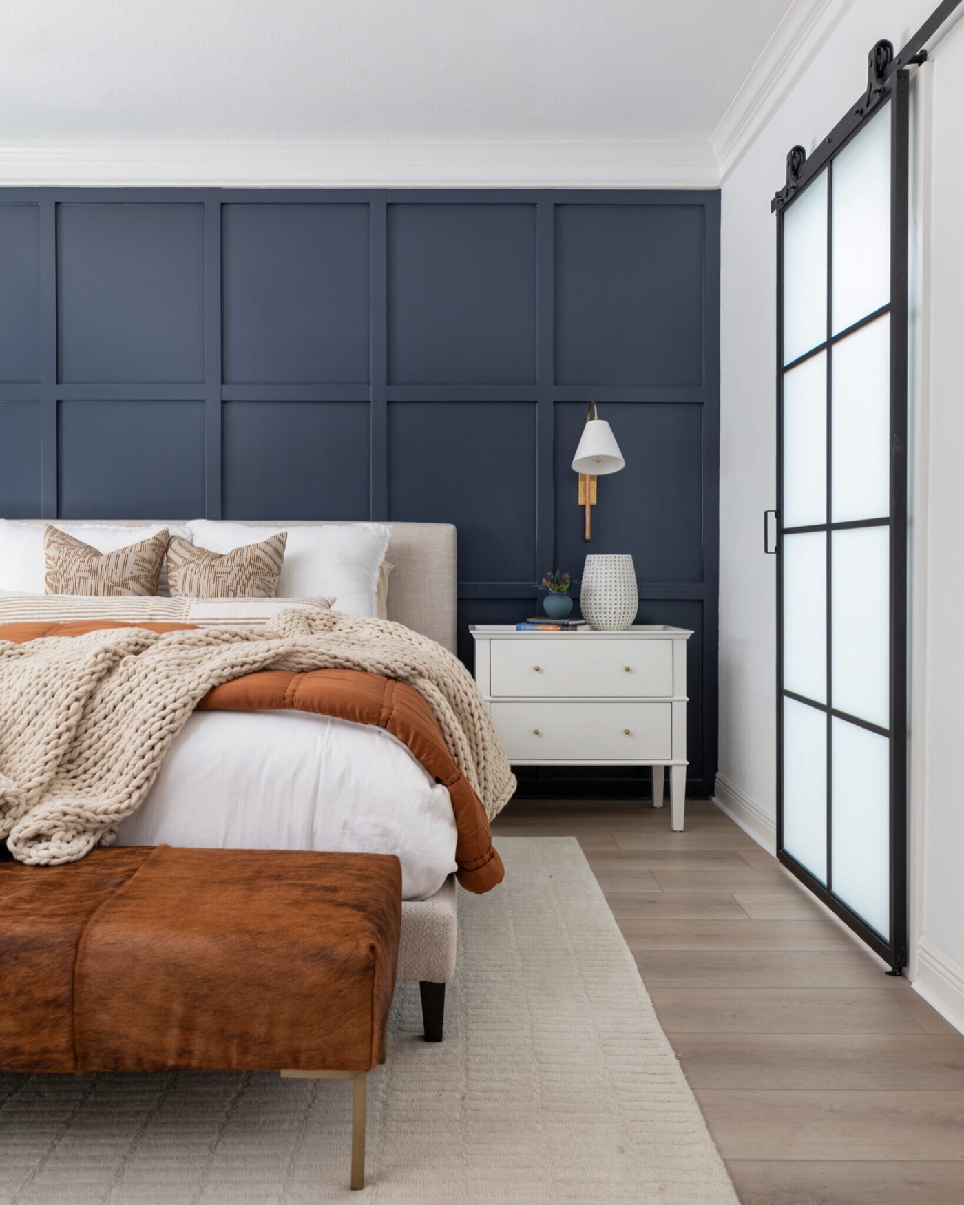 Navy panelled wall behind the bed beside a black steel and frosted glass barn door in the Evergreen Suite Bedroom project by Jennifer Kizzee Design