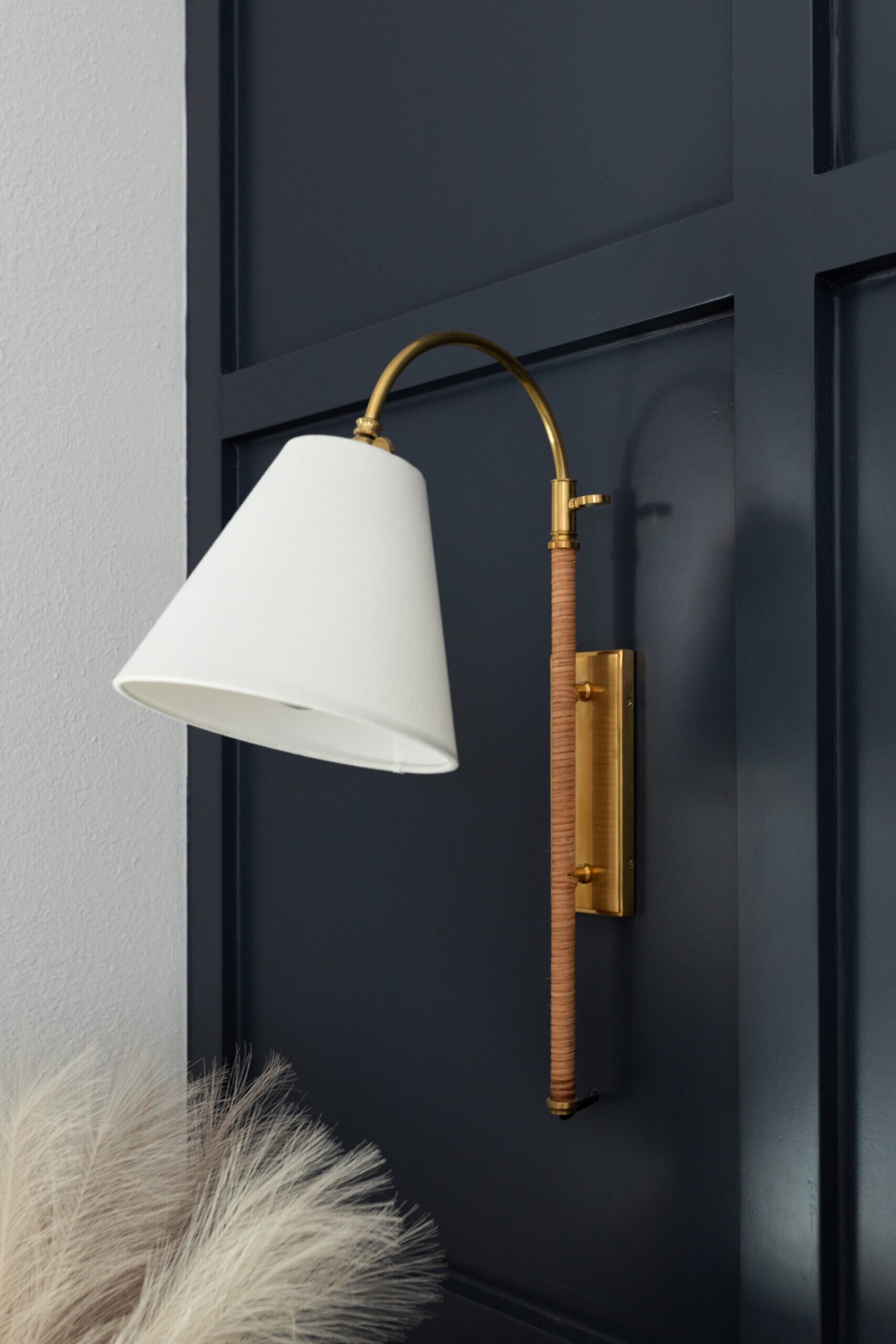 Aged brass wall sconce with a wrapped stem and white cone shade mounted on navy paneling in the Evergreen Suite Bedroom project by Jennifer Kizzee Design