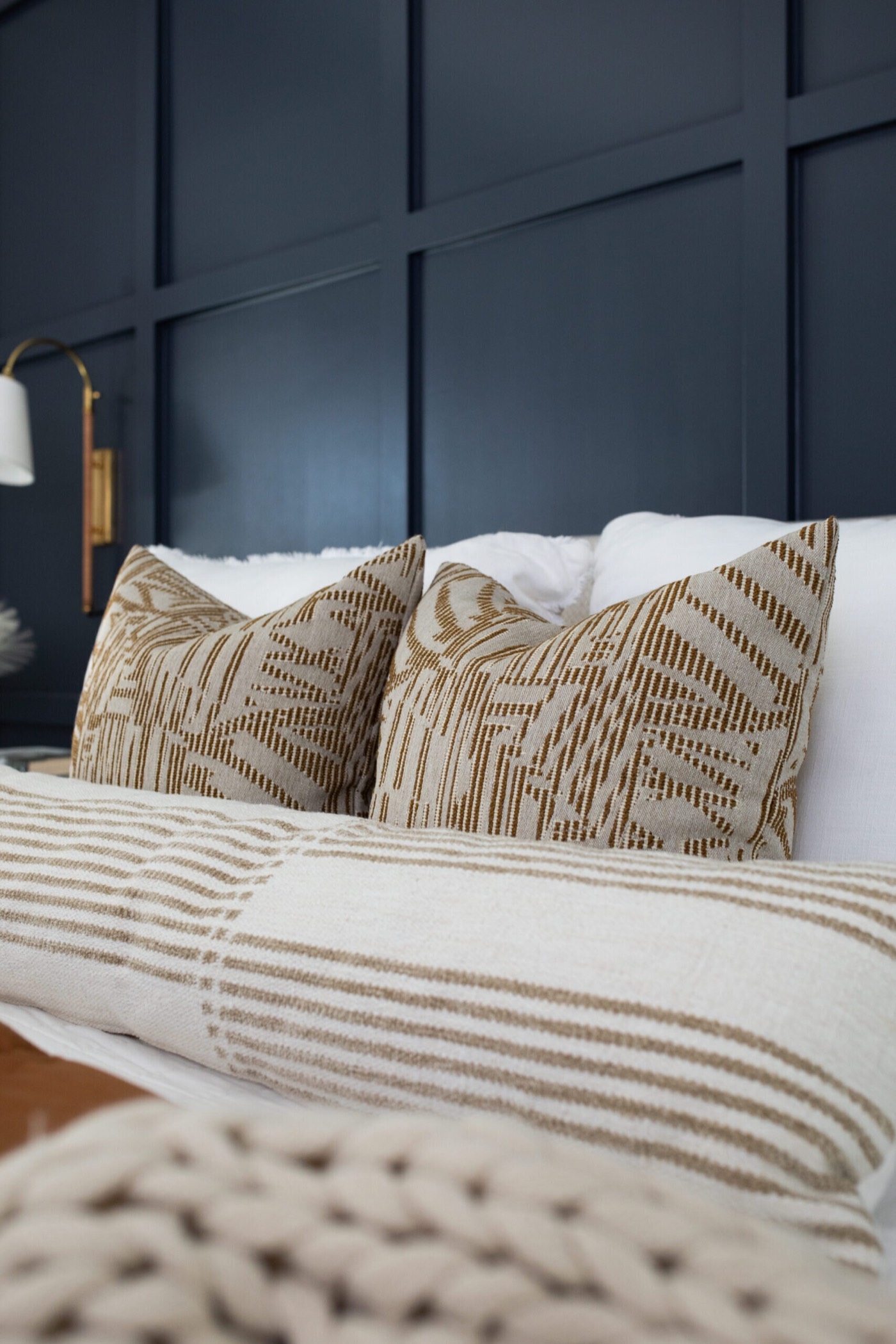 Camel geometric print pillows layered over cream striped shams against navy paneling in the Evergreen Suite Bedroom project by Jennifer Kizzee Design