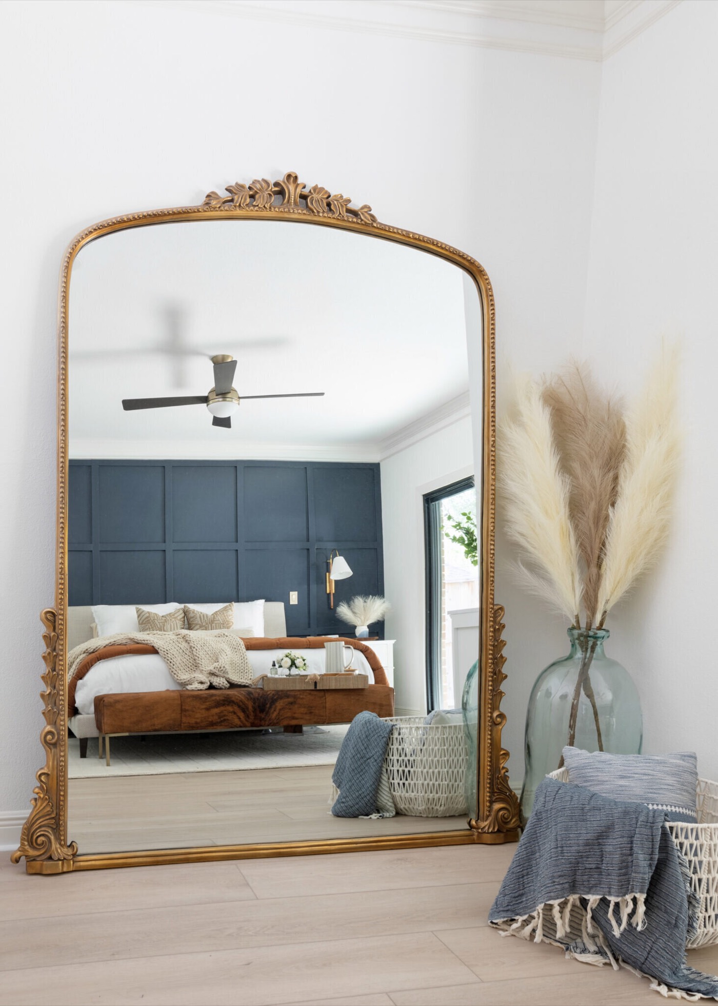 Ornate gold leaning floor mirror reflecting the bed and the navy panelled wall in the Evergreen Suite Bedroom project by Jennifer Kizzee Design