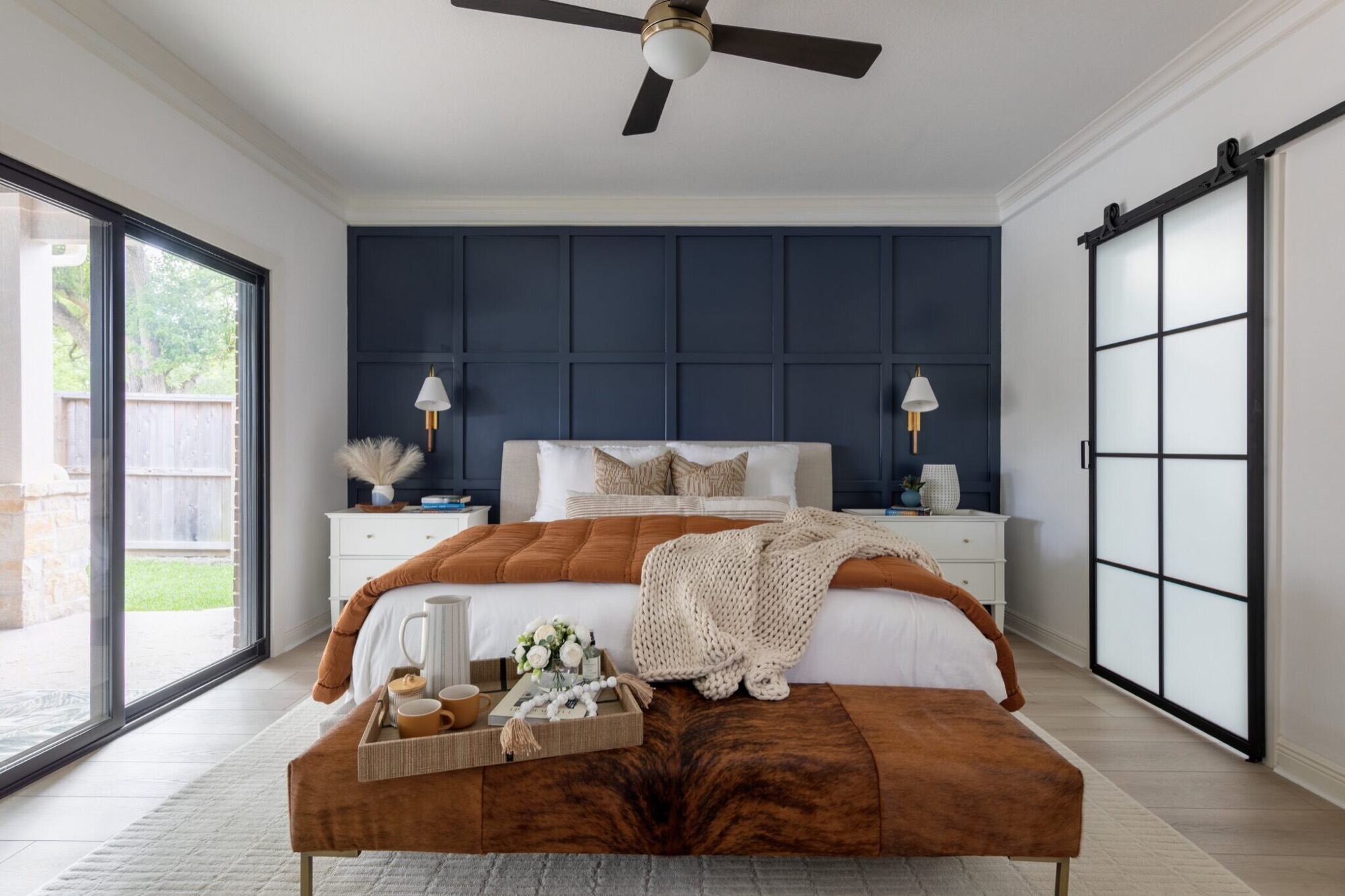 Upholstered bed against a floor-to-ceiling navy grid panel wall with a brindle hide bench at its foot in the Evergreen Suite Bedroom project by Jennifer Kizzee Design