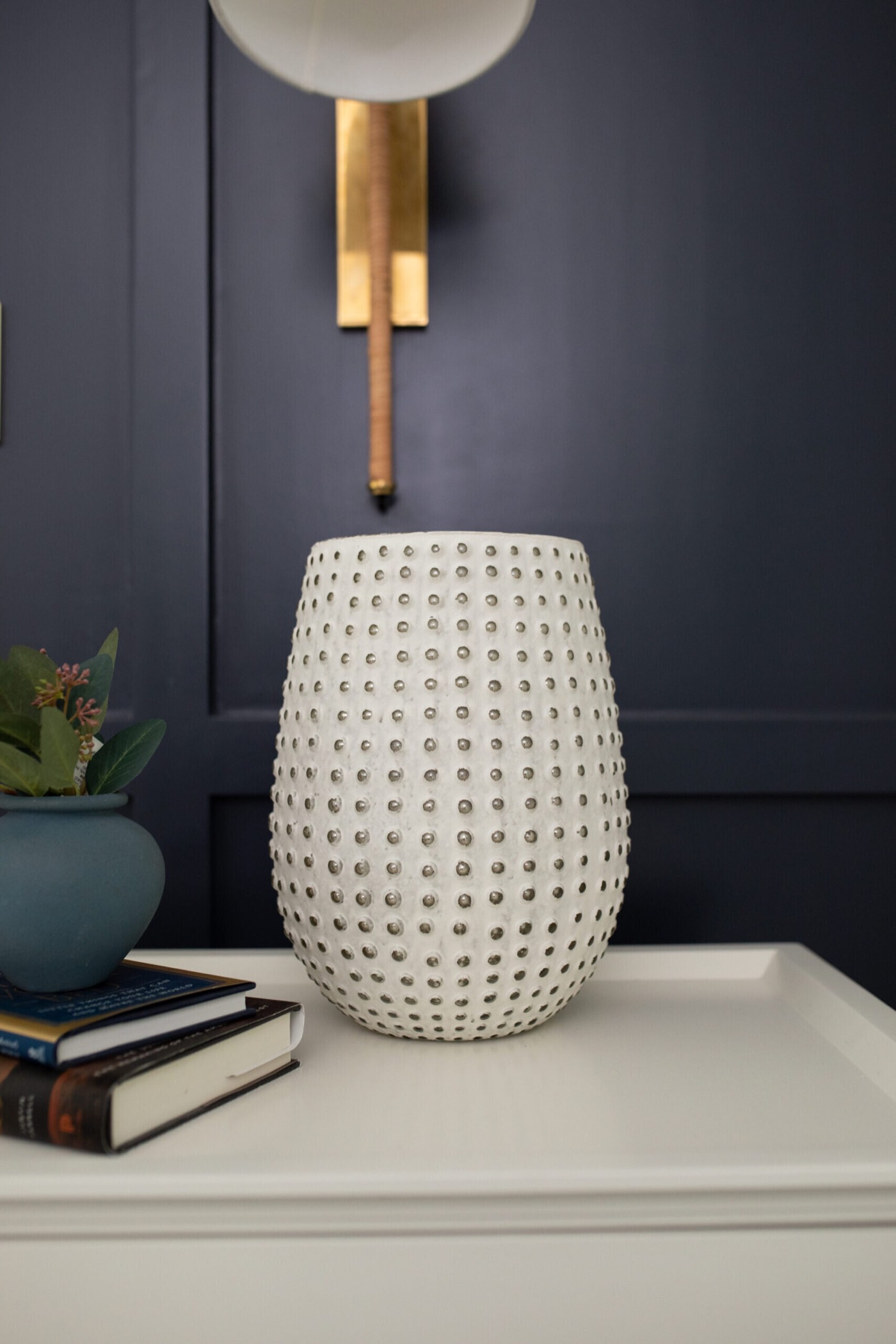 White dotted ceramic vase on the nightstand below an aged brass sconce in the Evergreen Suite Bedroom project by Jennifer Kizzee Design