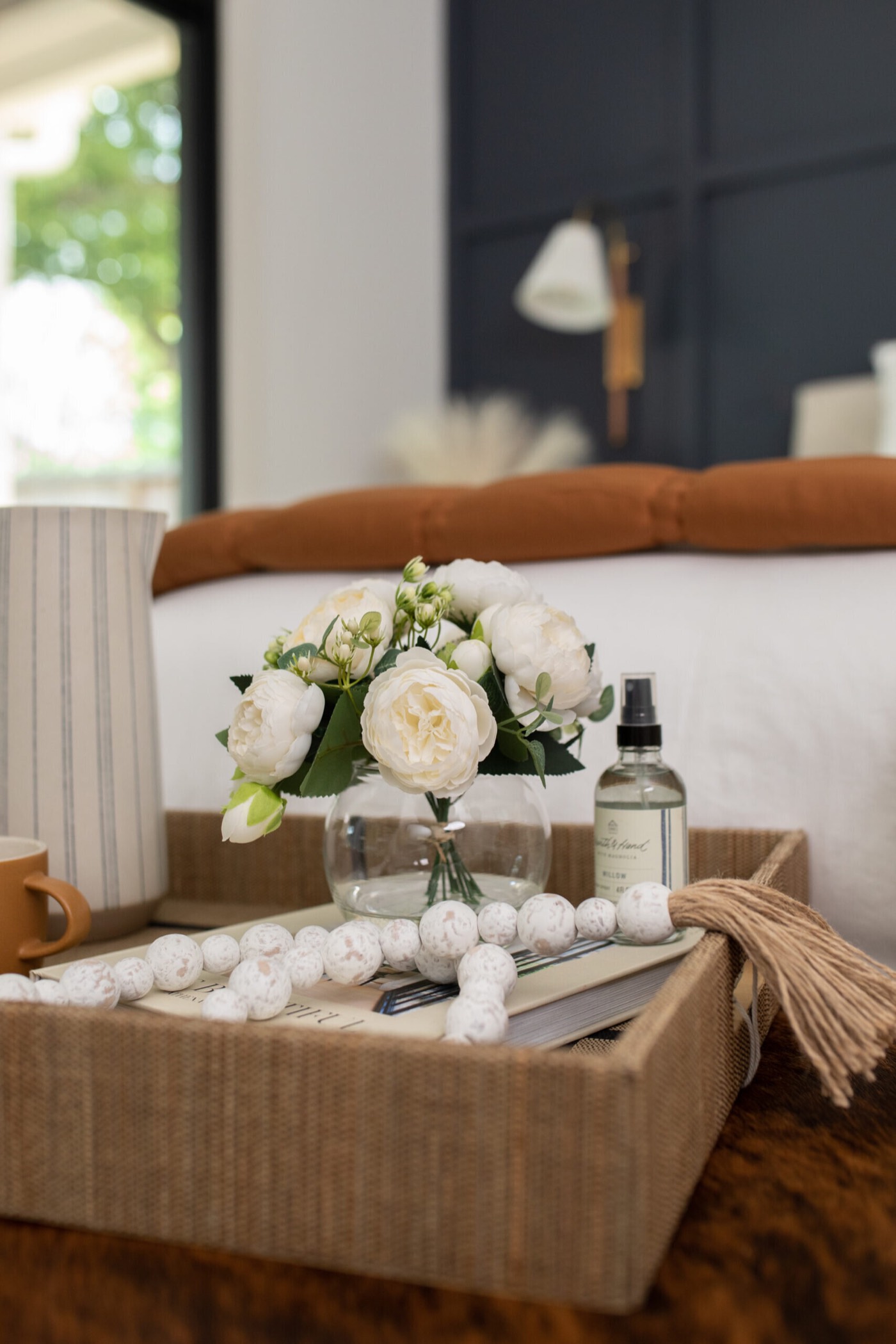 Woven tray with white peonies styled on the brindle hide bench at the foot of the bed in the Evergreen Suite Bedroom project by Jennifer Kizzee Design