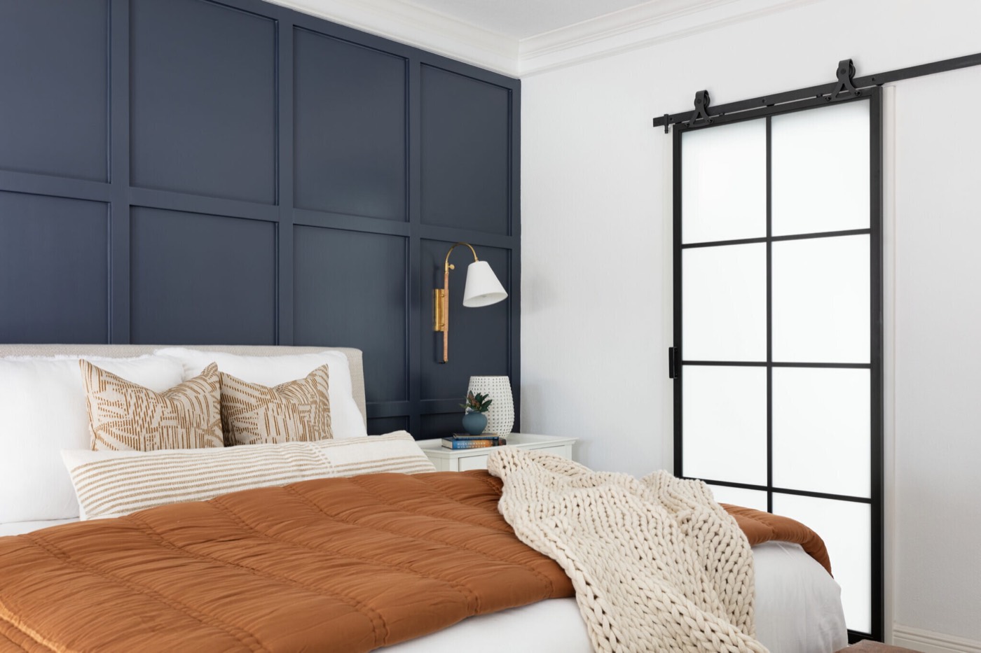 Rust quilted coverlet and cream chunky knit throw on the bed beside the black steel barn door in the Evergreen Suite Bedroom project by Jennifer Kizzee Design