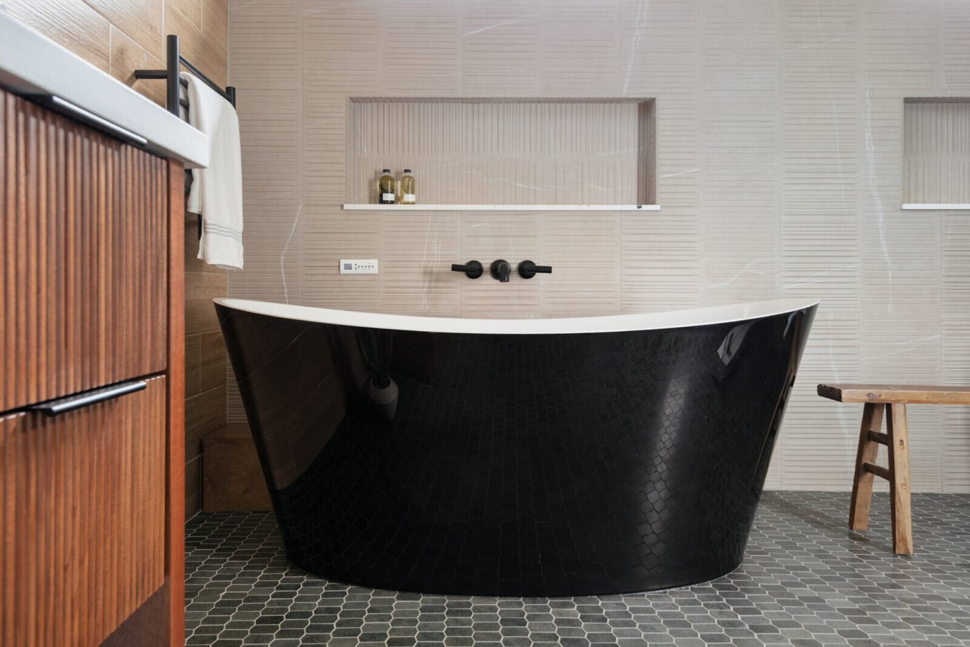 Black freestanding tub against wood look tile under a black wall filler in the Fox Run Modern Bath project by Jennifer Kizzee Design