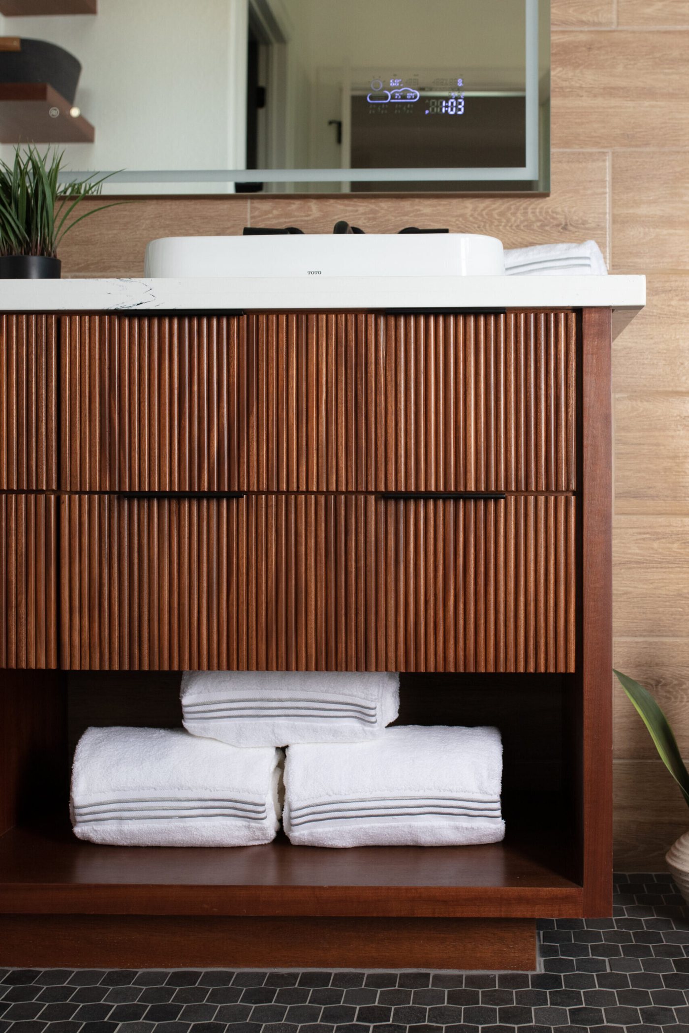Fluted walnut vanity with a shelf of folded towels underneath in the Fox Run Modern Bath project by Jennifer Kizzee Design