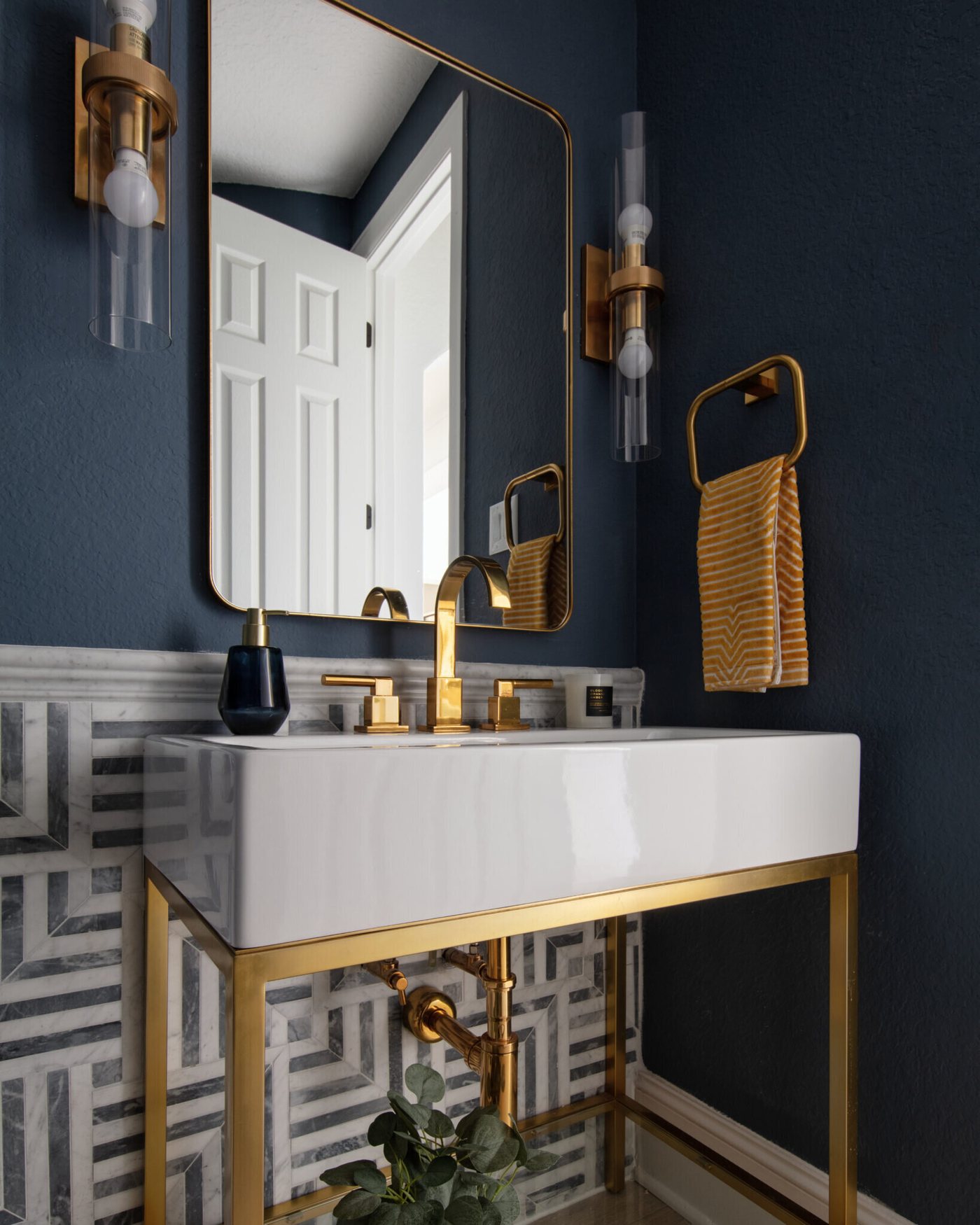 Navy powder room with a brass console sink, a geometric floor and brass sconces in the Fox Run Modern Bath project by Jennifer Kizzee Design