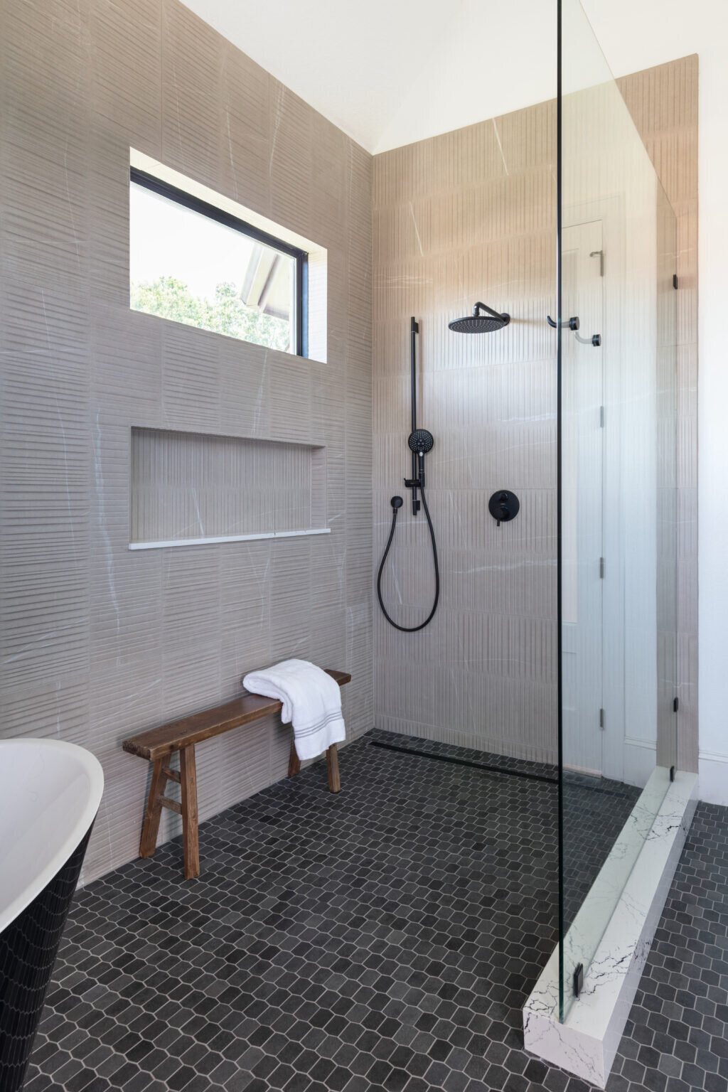 Walk-in shower in wood look tile with matte black fittings and a wood bench in the Fox Run Modern Bath project by Jennifer Kizzee Design