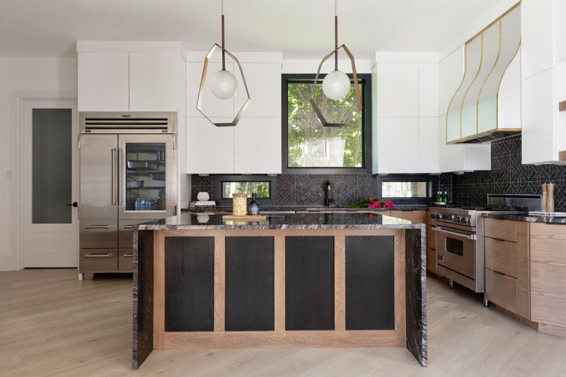 Black stone island with a waterfall edge under faceted pendants in a walnut kitchen in the Fox Run Modern Kitchen project by Jennifer Kizzee Design