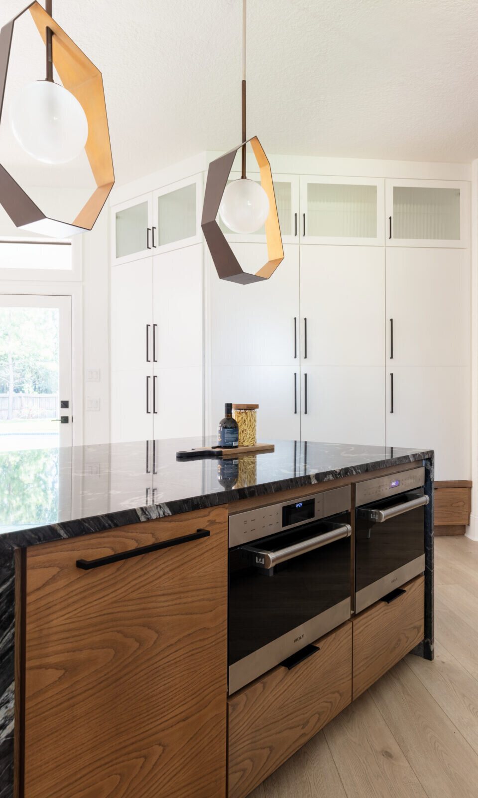 Faceted brass pendants hung over the black stone island in the Fox Run Modern Kitchen project by Jennifer Kizzee Design