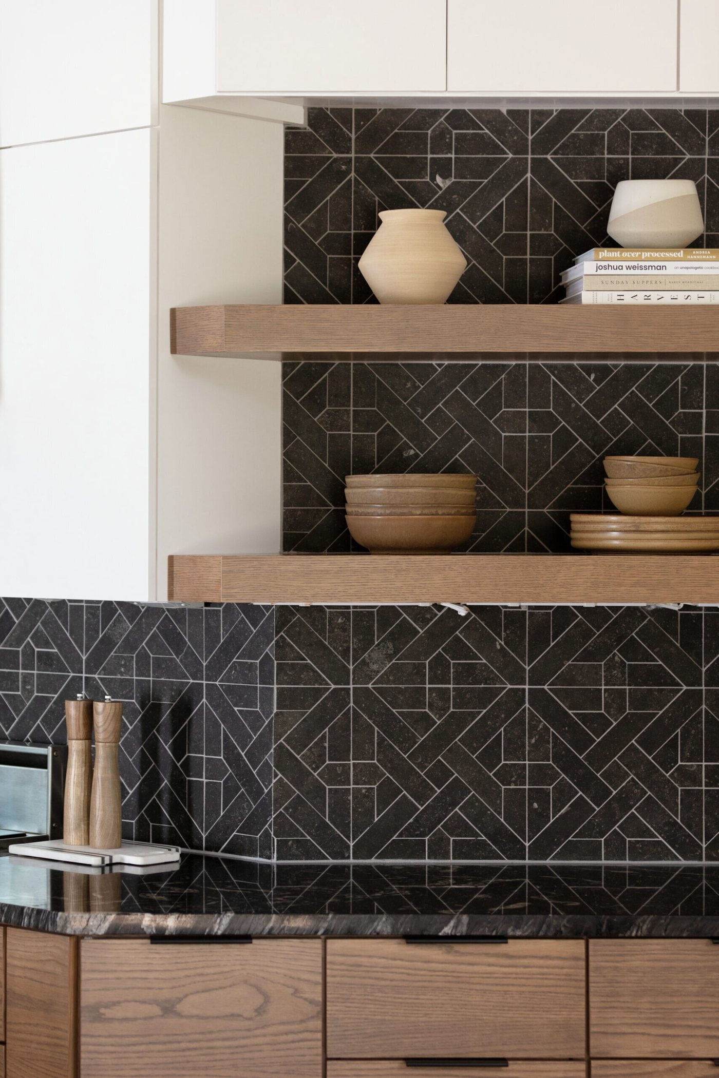 Open walnut shelves against black geometric tile holding ceramics in the Fox Run Modern Kitchen project by Jennifer Kizzee Design