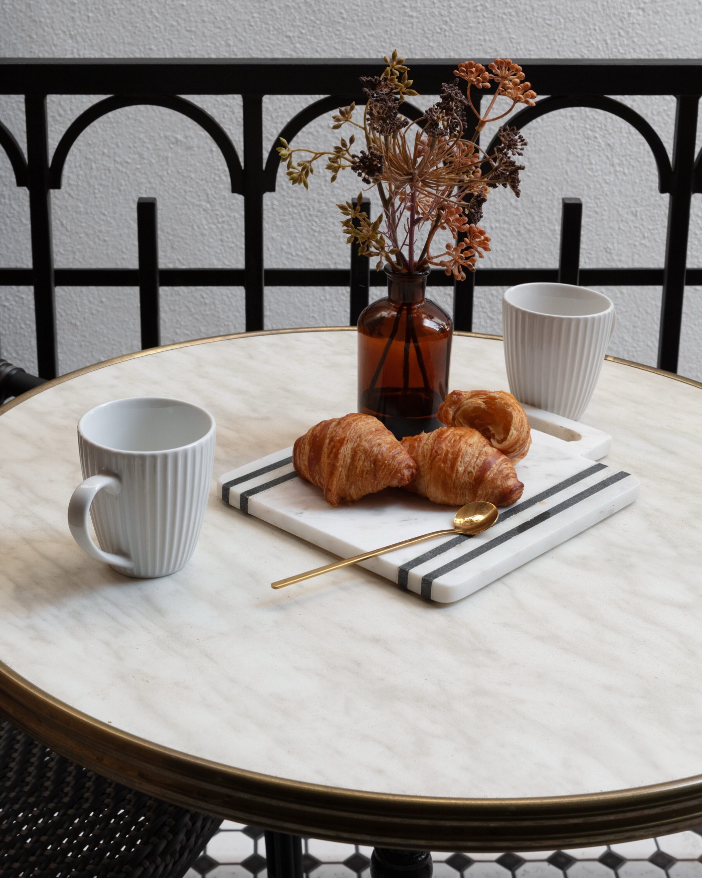 Balcony bistro table in marble with a brass edge, set with coffee cups above a black iron railing in the Gateway Condo project by Jennifer Kizzee Design