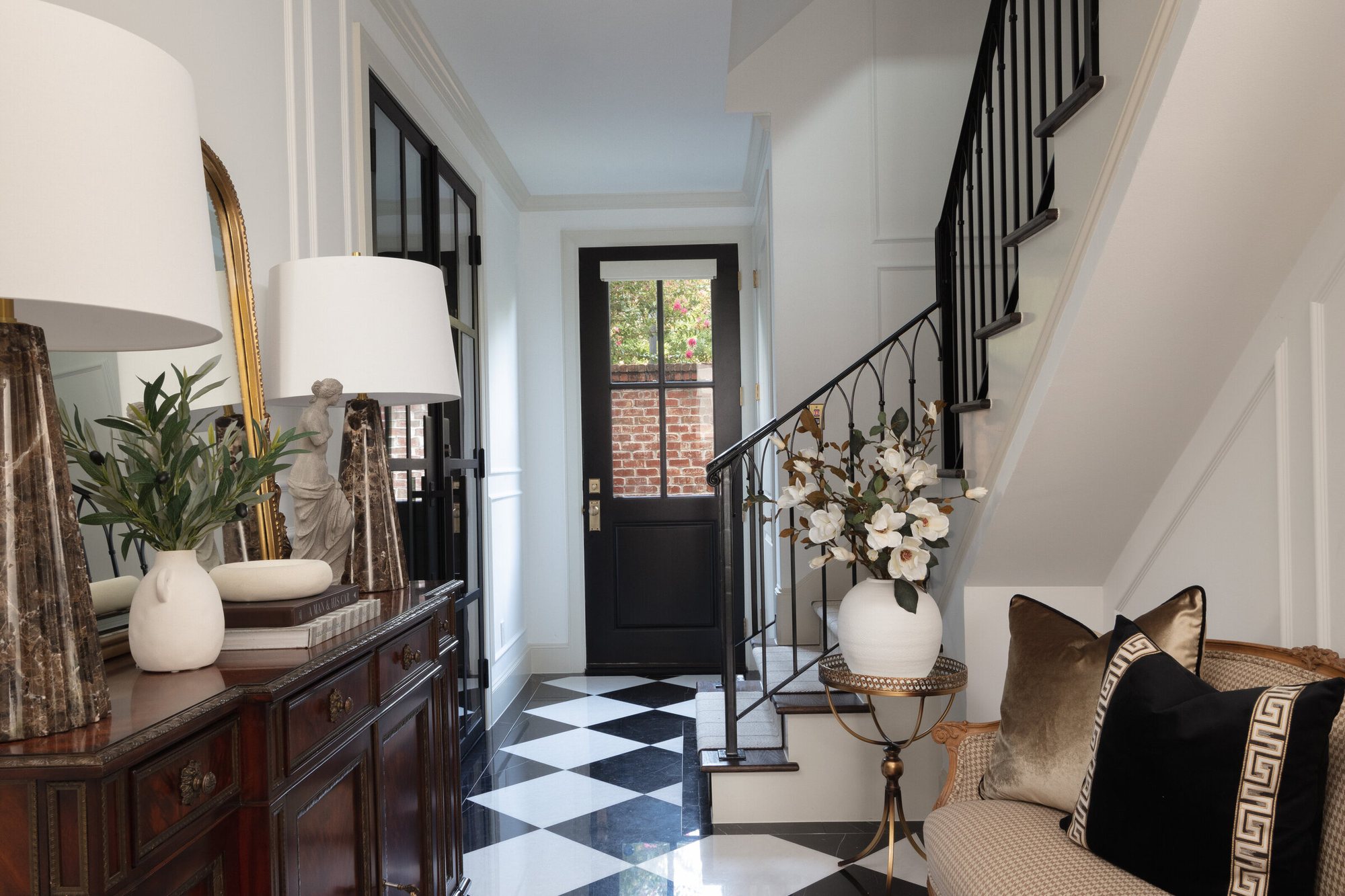 Entry hall with a black and white checkerboard marble floor and a dark staircase in the Gateway Condo project by Jennifer Kizzee Design