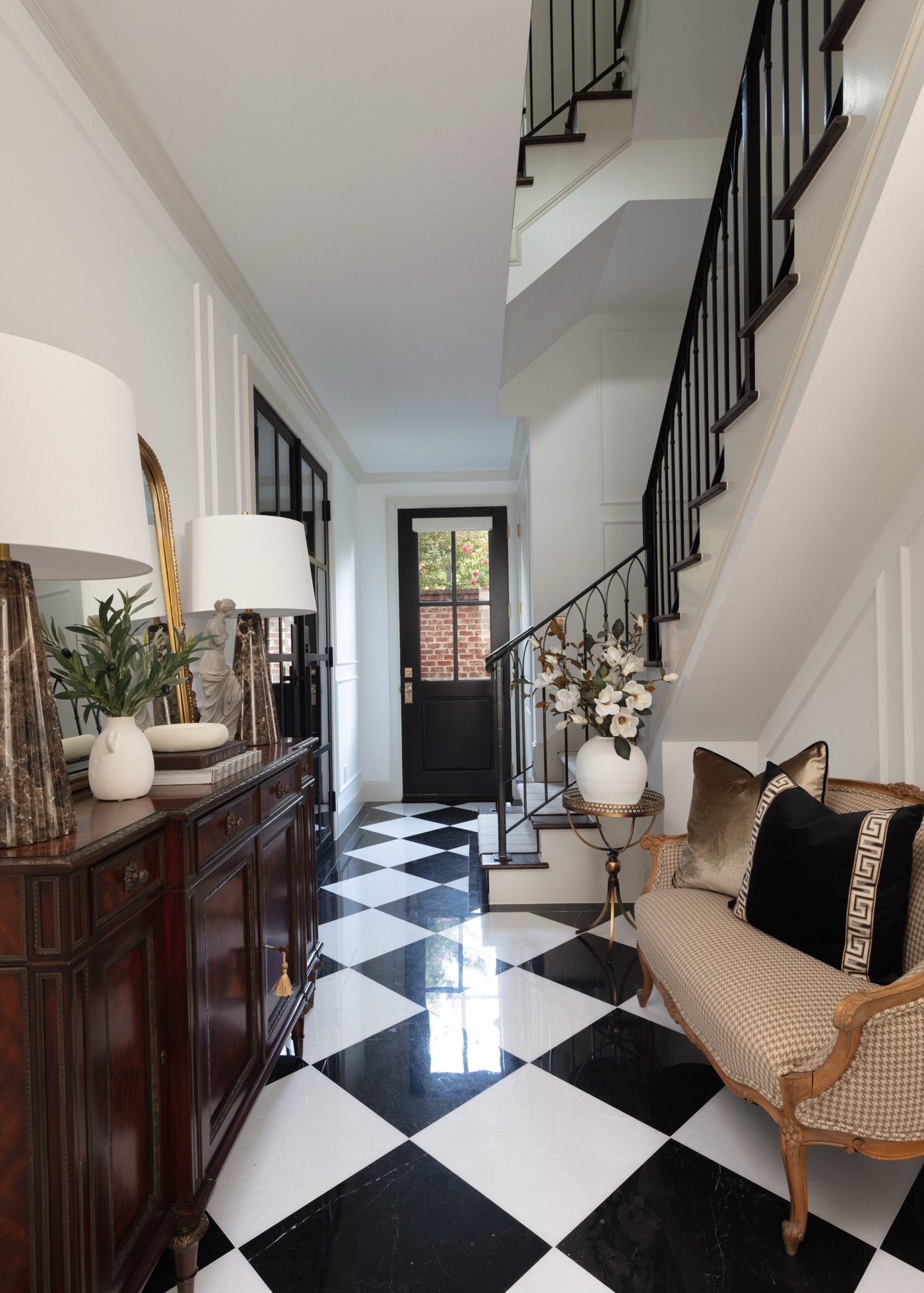 Entry hall with a black and white checkerboard marble floor and a black staircase with slim iron balusters in the Gateway Condo project by Jennifer Kizzee Design