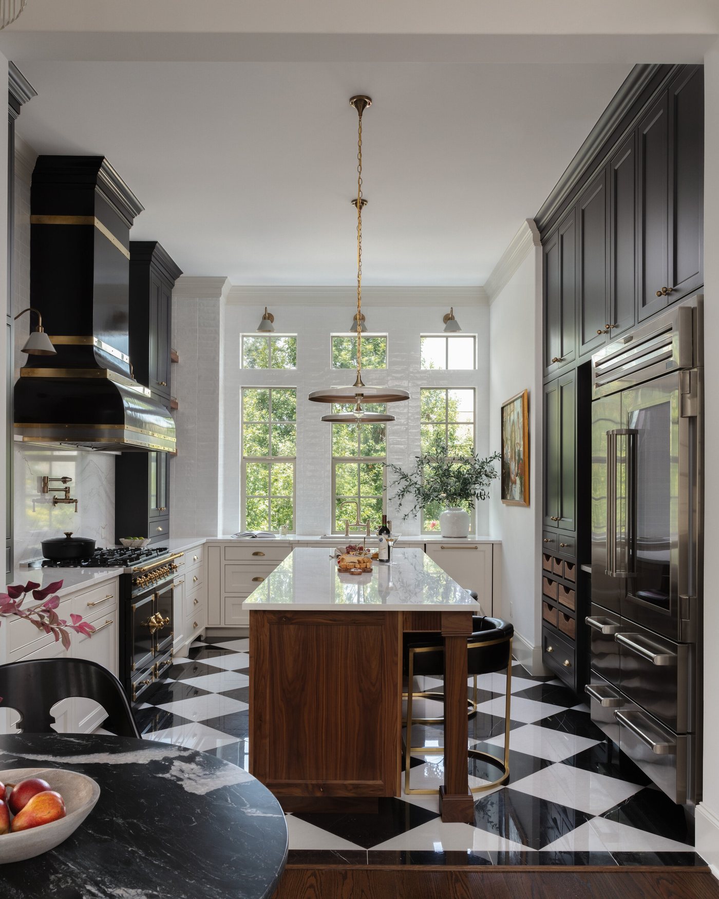 Kitchen with black cabinetry, a brass-banded hood and a walnut island over a black and white checkerboard marble floor in the Gateway Condo project by Jennifer Kizzee Design in The Woodlands, Texas