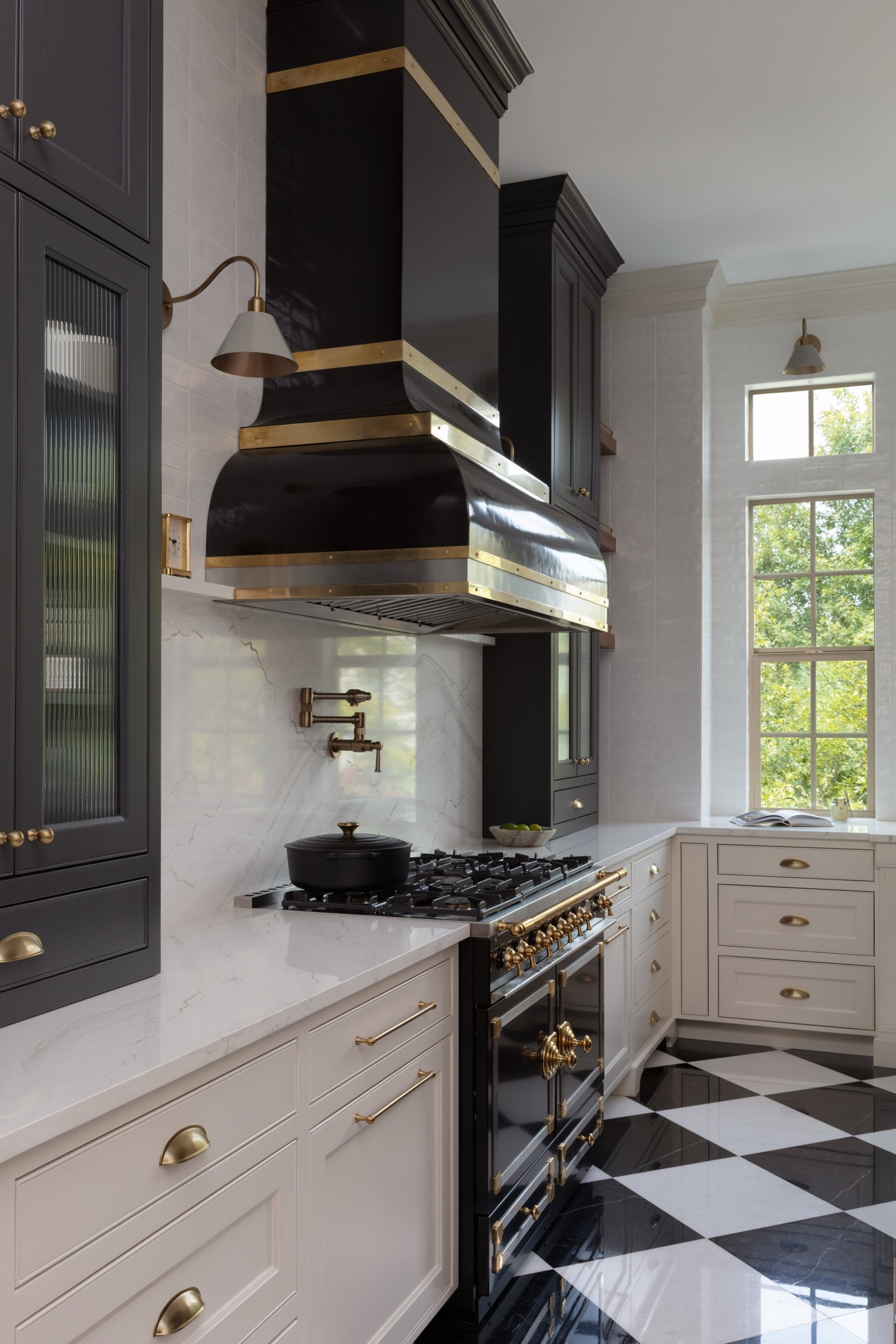 Kitchen with a black lacquer range hood banded in brass above a range, set against white marble in the Gateway Condo project by Jennifer Kizzee Design