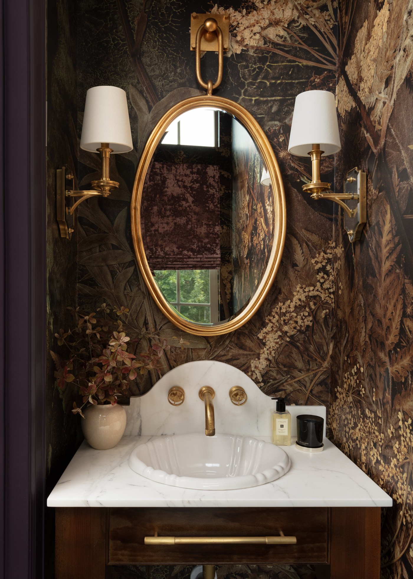Powder room wrapped in a dark botanical mural wallpaper with a gilt oval mirror above a marble sink deck in the Gateway Condo project by Jennifer Kizzee Design