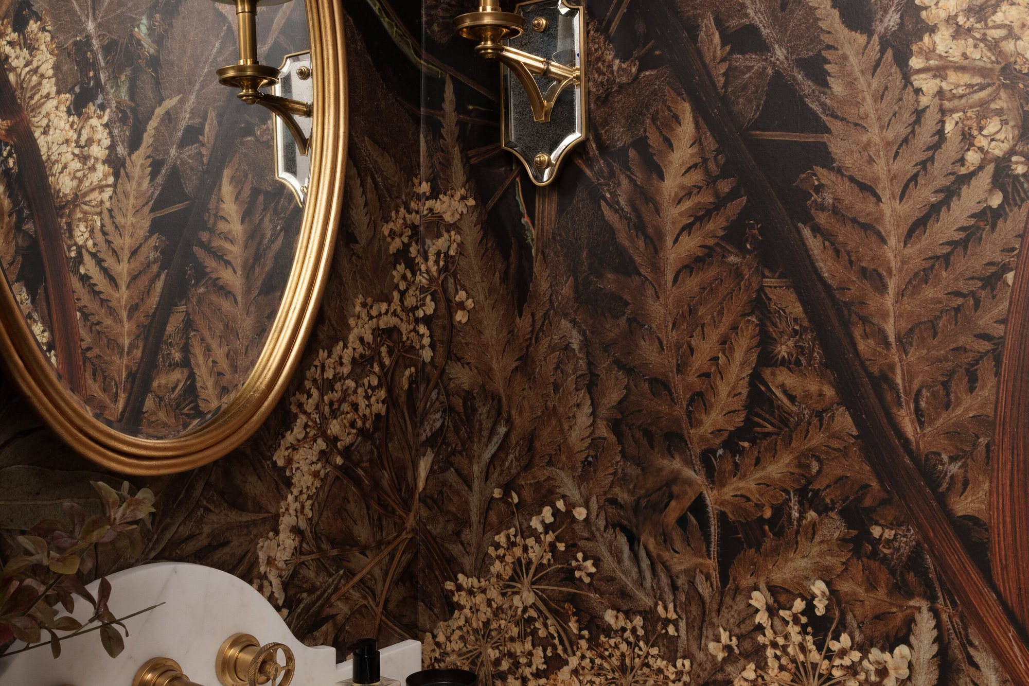 Powder room with a dark botanical mural, a gold oval mirror and a wall-mounted brass faucet in the Gateway Condo project by Jennifer Kizzee Design