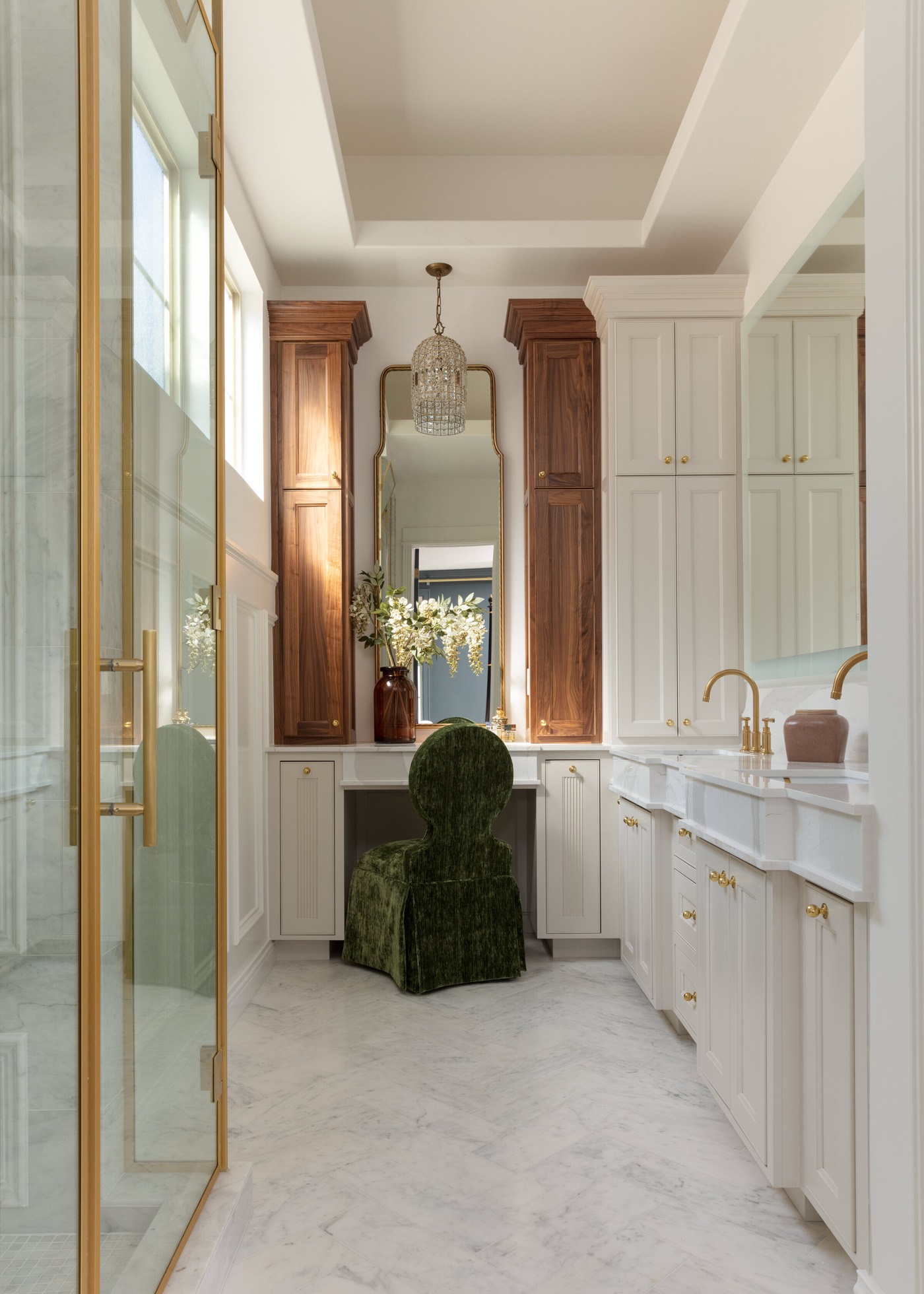 Primary bathroom with cream inset cabinetry between walnut storage towers, a glass shower, and a crystal lantern overhead in the Gateway Condo project by Jennifer Kizzee Design