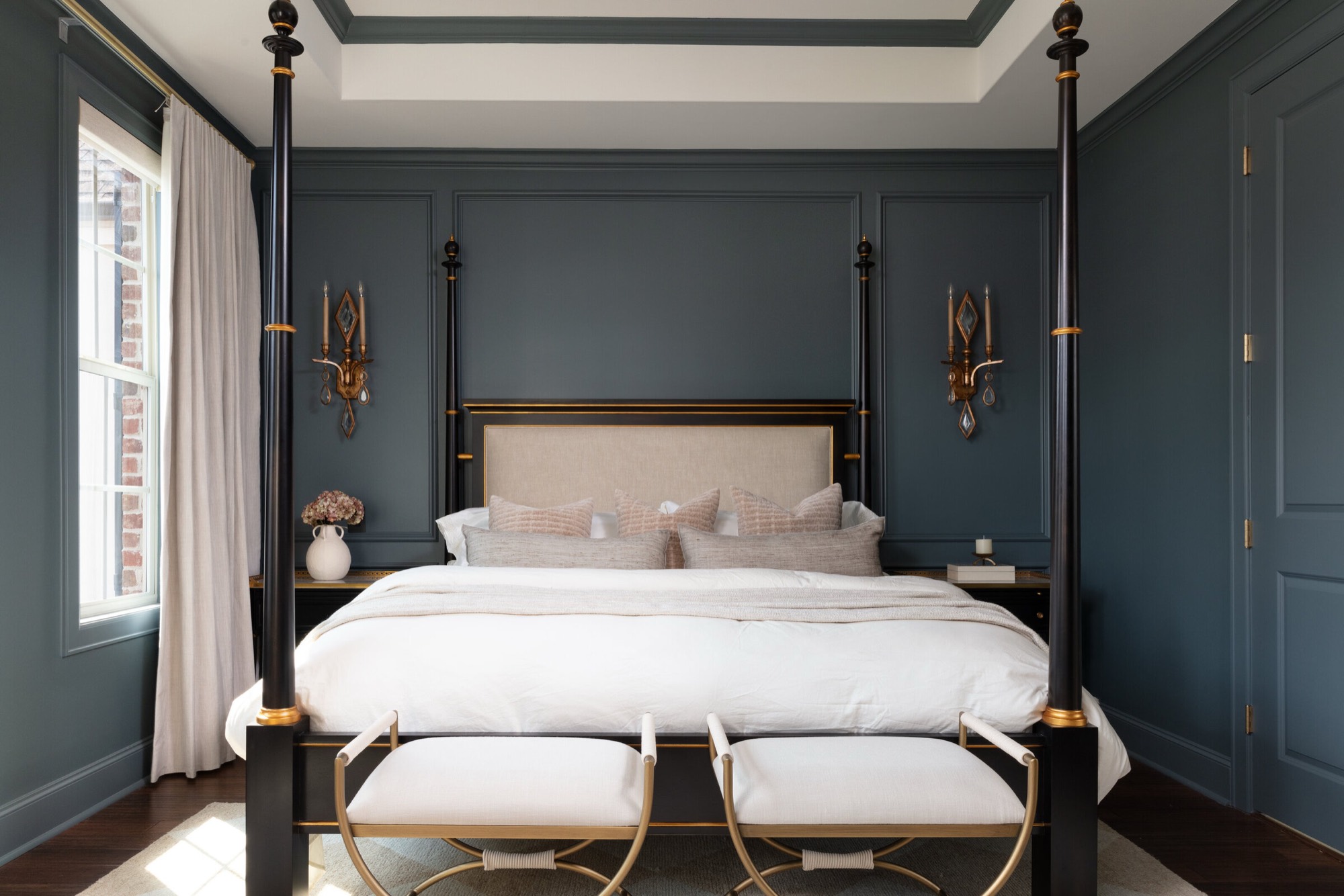 Primary bedroom with dark teal paneled walls around a black and gilt four-poster bed flanked by gilt sconces in the Gateway Condo project by Jennifer Kizzee Design