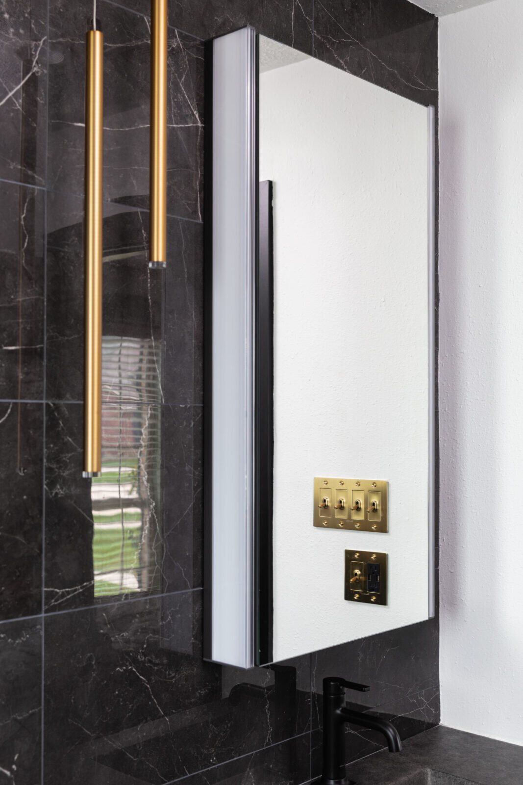 Brass strip lights flanking a mirror on a black marble wall in the Gentleman's Retreat project by Jennifer Kizzee Design