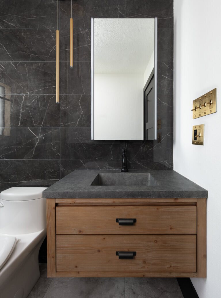 Floating cedar vanity with a stone basin against a black marble wall in the Gentleman's Retreat project by Jennifer Kizzee Design