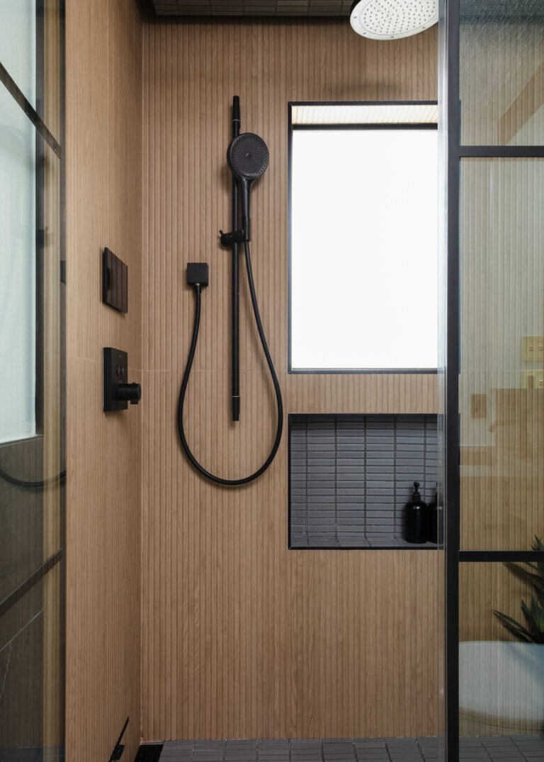 Matte black shower fittings on a slatted wood wall beside a window in the Gentleman's Retreat project by Jennifer Kizzee Design