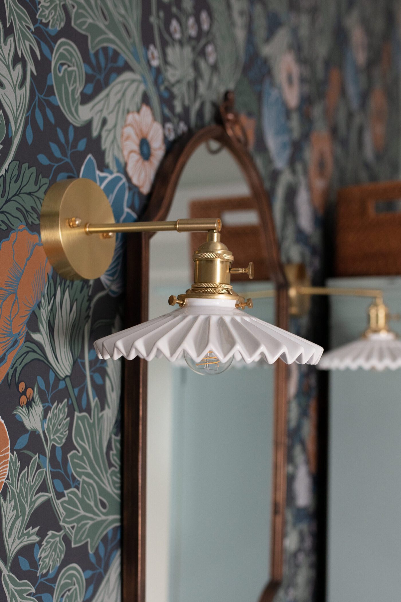 Brass swing arm sconce with a fluted milk glass shade on floral wallpaper in the Heights Primary Bath project by Jennifer Kizzee Design