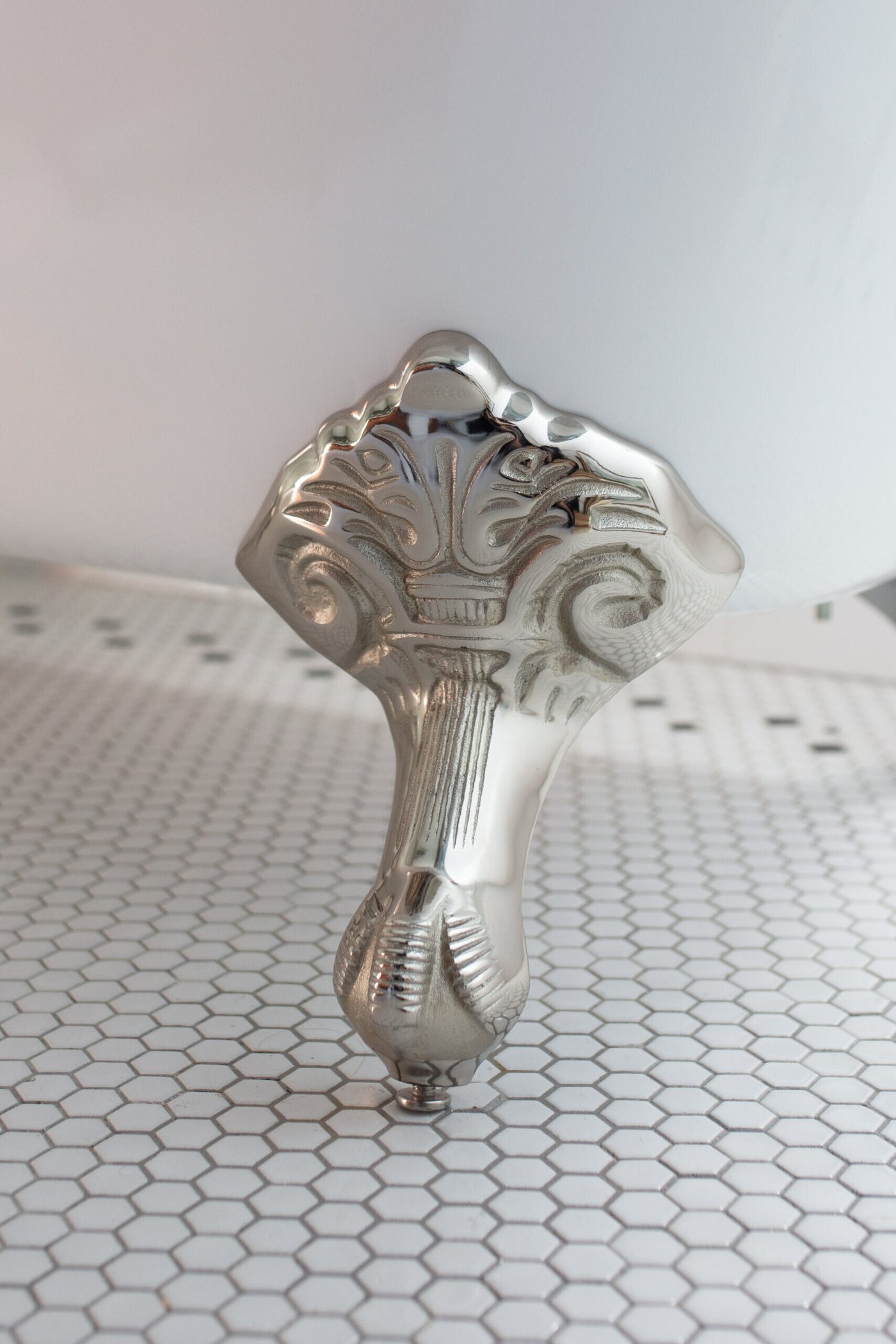 Polished nickel clawfoot tub foot on a white hex mosaic floor in the Heights Primary Bath project by Jennifer Kizzee Design