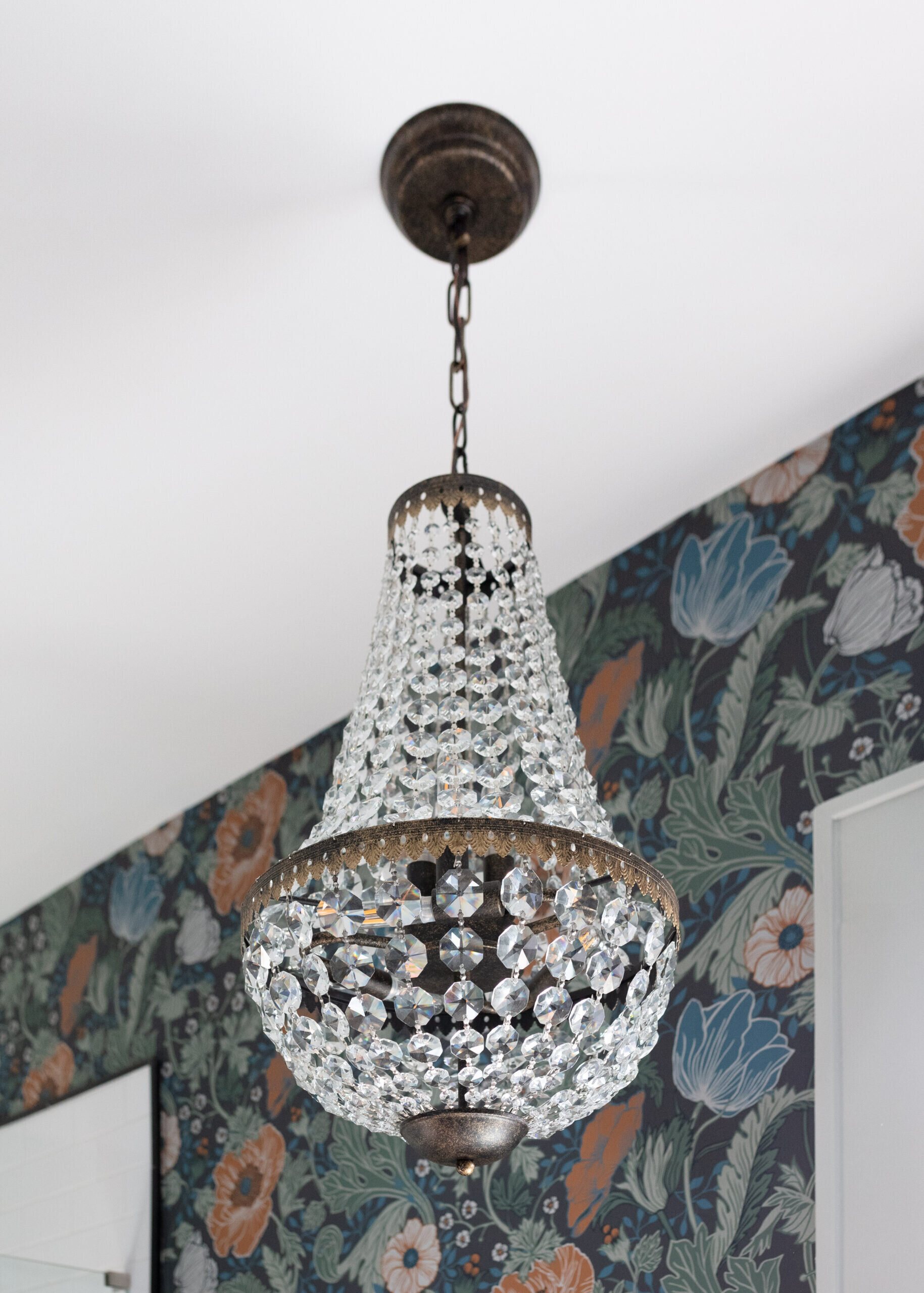 Walnut double vanity with marble counters, arched mirrors and brass swing arm sconces against floral wallpaper in the Heights Primary Bath project by Jennifer Kizzee Design