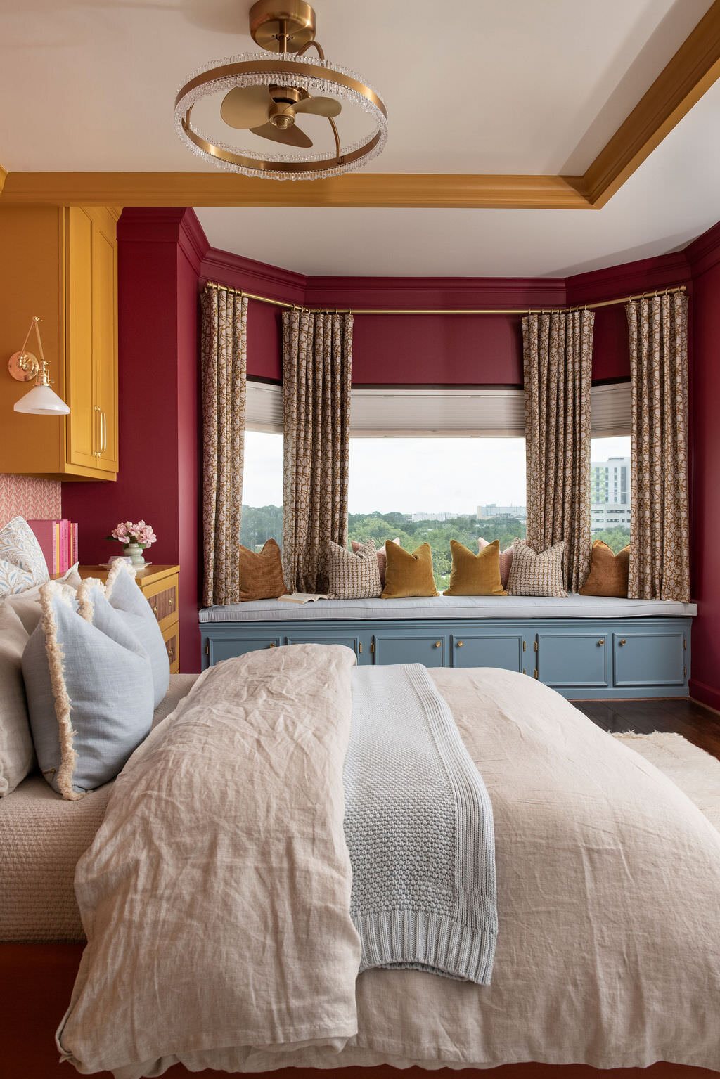 Bedroom window seat in blue beneath a bay of windows with burgundy walls in the Holcombe Condo project by Jennifer Kizzee Design