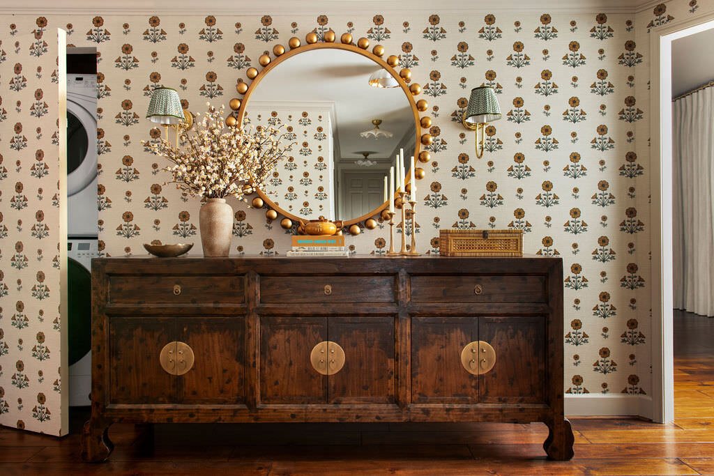 Block print wallpaper above an antique chest with brass medallions in the Holcombe Condo project by Jennifer Kizzee Design