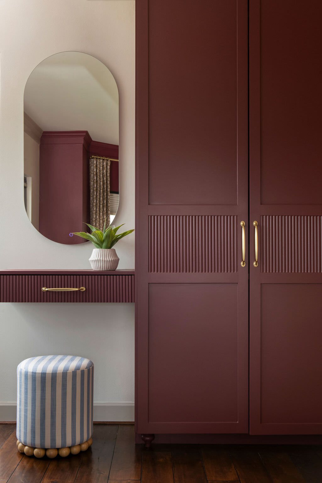 Burgundy fluted wardrobe doors beside an arched mirror and a striped stool in the Holcombe Condo project by Jennifer Kizzee Design