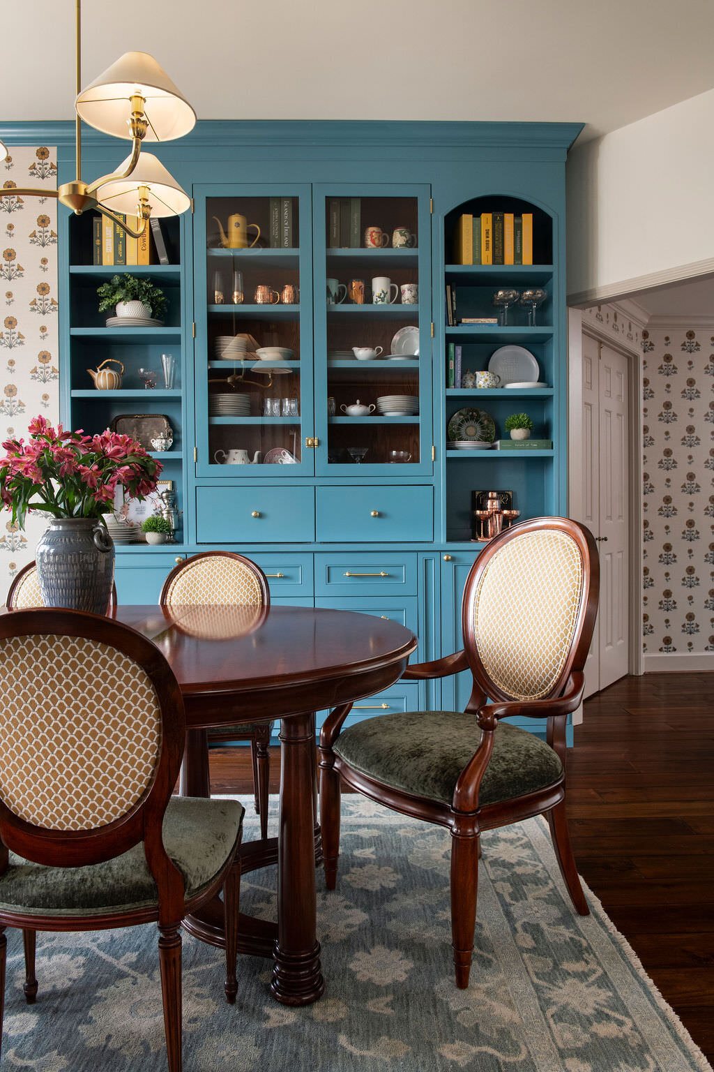Dining room with bright blue glass front built-ins and cane back chairs in the Holcombe Condo project by Jennifer Kizzee Design