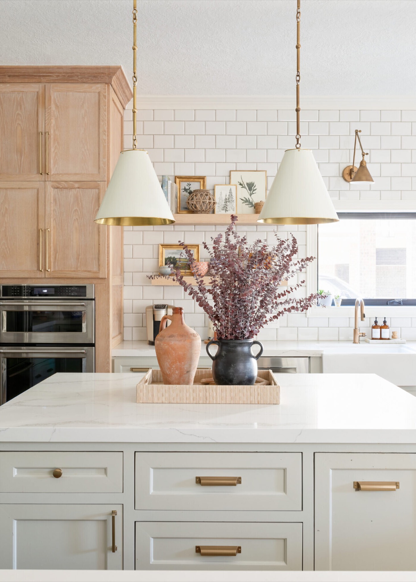 Kitchen island in pale veined stone with brass bar pulls beneath a pair of brass capped cone pendants in the Jenn's Kitchen project by Jennifer Kizzee Design