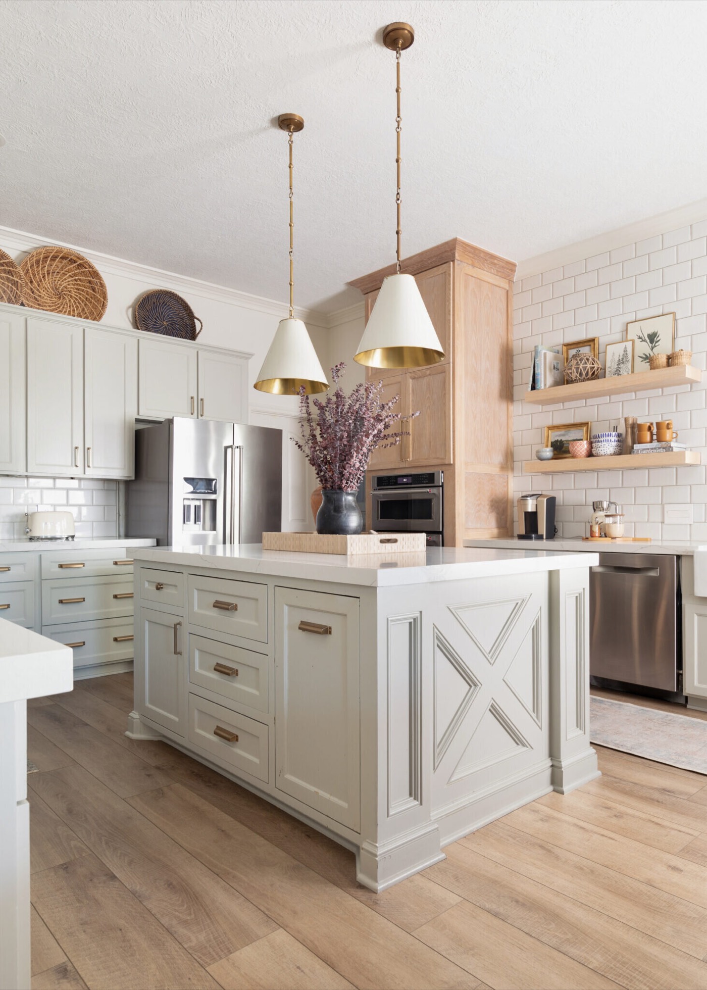 Kitchen island with an applied X brace end panel under two brass capped cone pendants, facing a white oak hood and open shelves in the Jenn's Kitchen project by Jennifer Kizzee Design