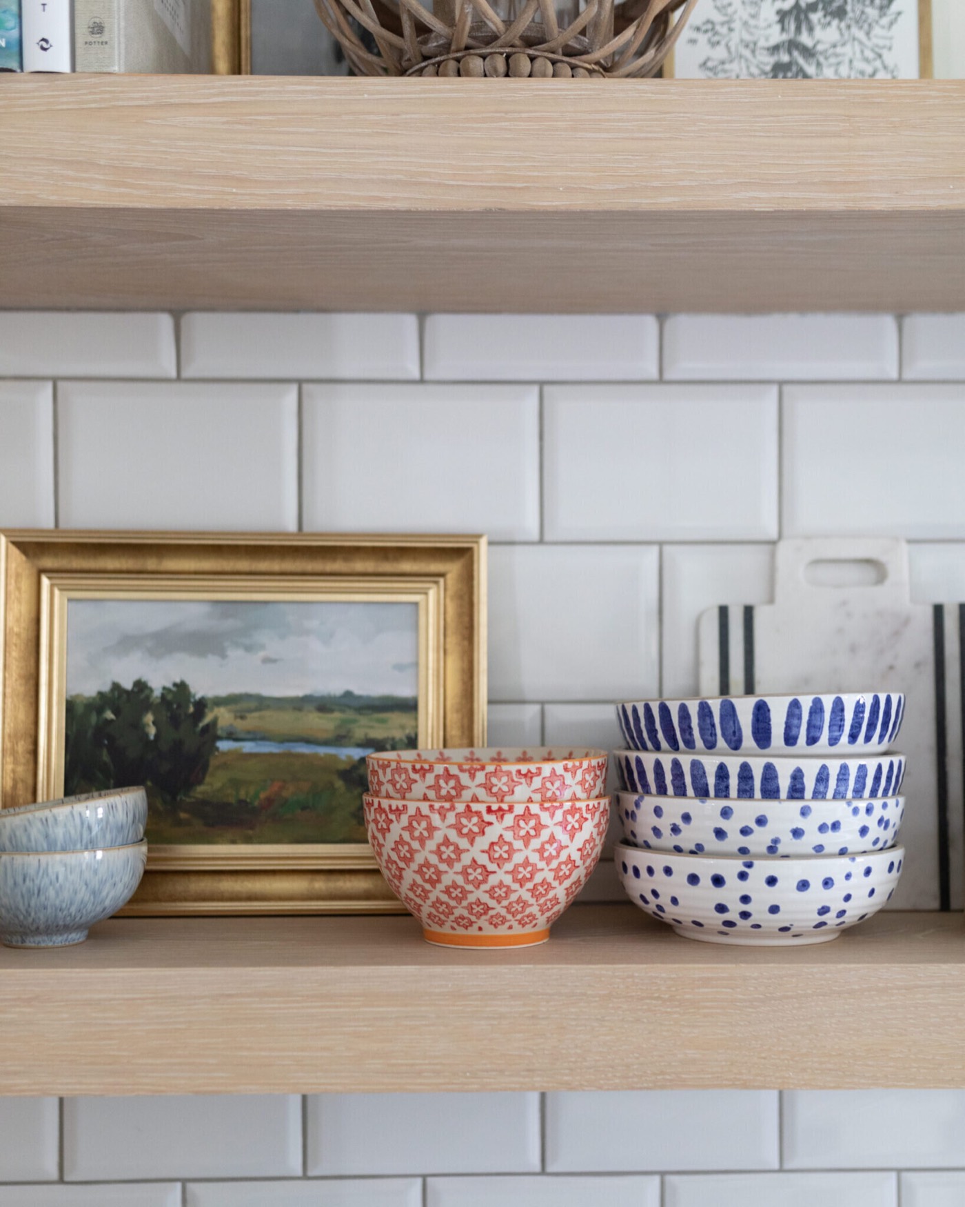 White oak floating shelf styled with a gilt framed landscape and blue and white bowls against white handmade tile in the Jenn's Kitchen project by Jennifer Kizzee Design