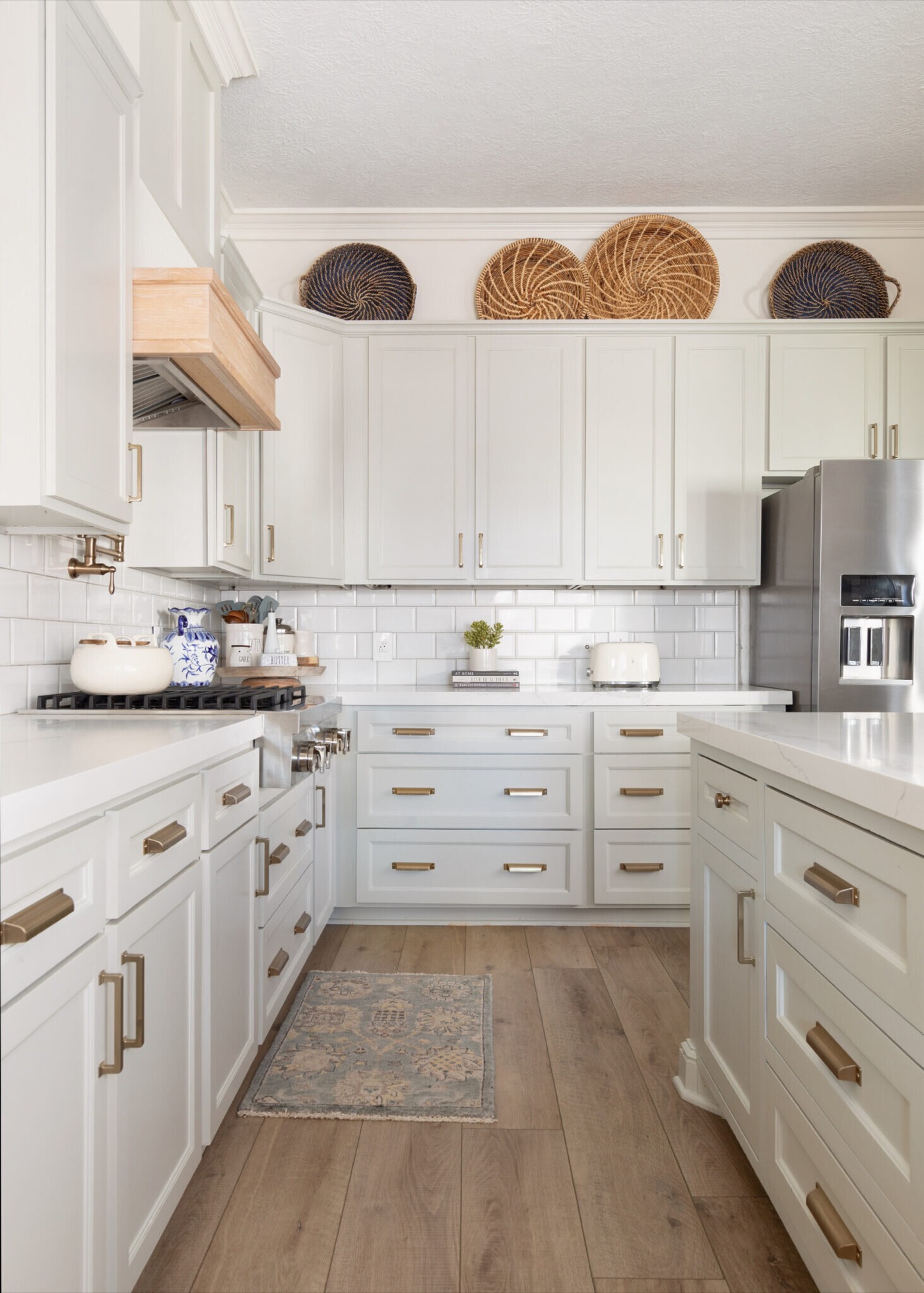 Kitchen perimeter run of shaker cabinetry with brass bar pulls under full height white tile, with the white oak hood at the range, in the Jenn's Kitchen project by Jennifer Kizzee Design