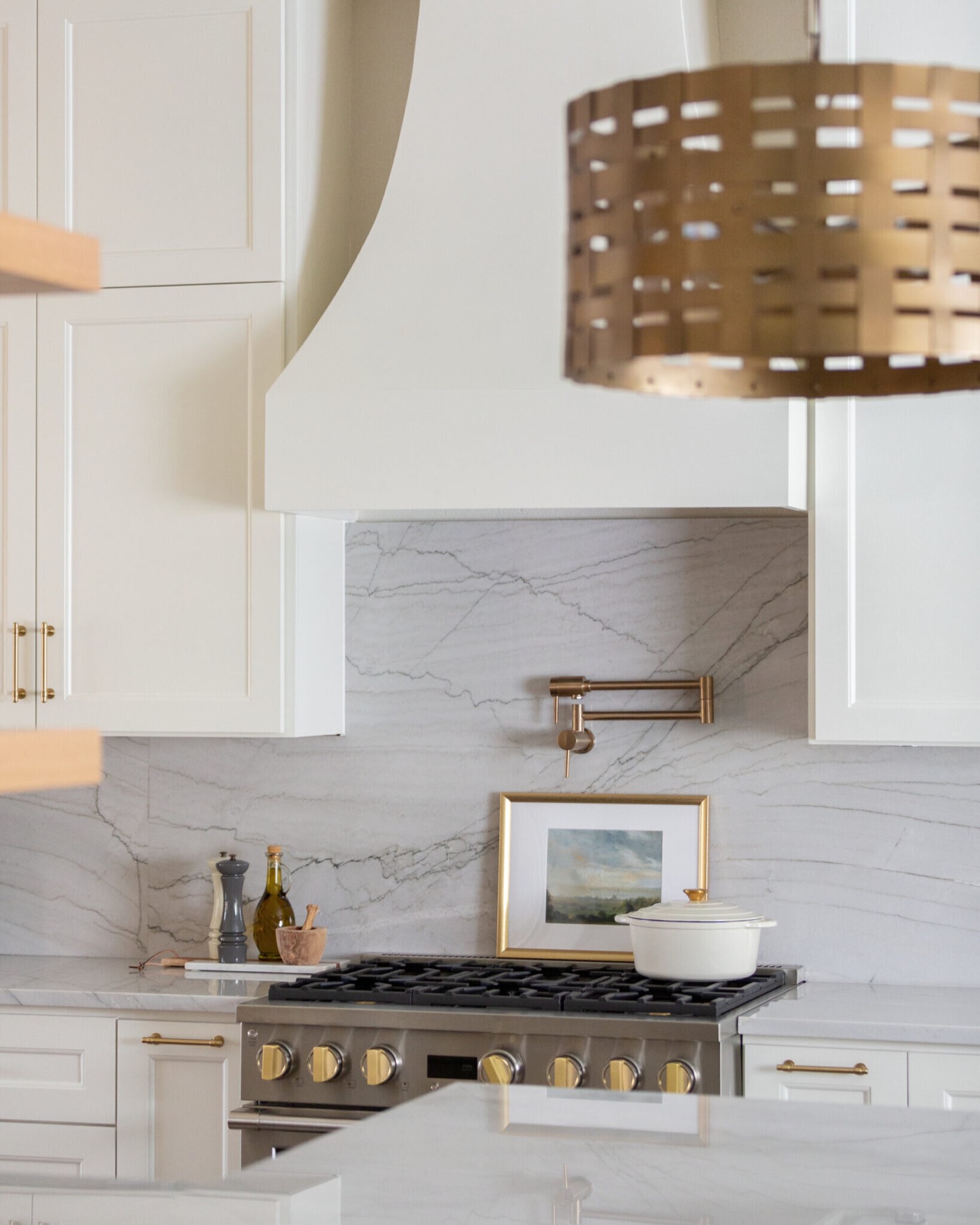 Gray veining in the marble slab backsplash behind a brass pot filler and the brass knobs of the range in the Knoll Kitchen project by Jennifer Kizzee Design