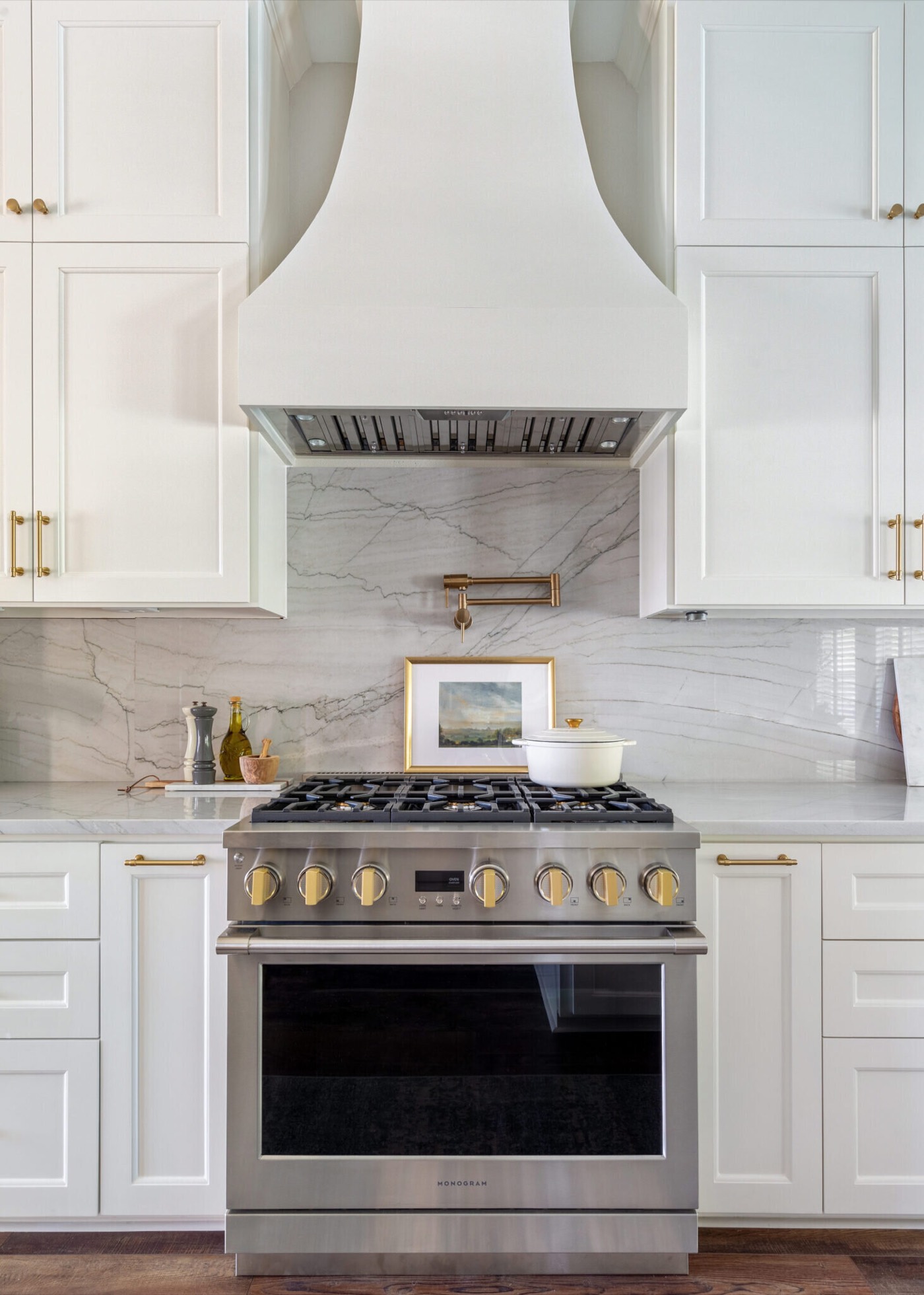 Painted range hood with a curved apron above a stainless pro range with brass knobs and a full height marble slab backsplash in the Knoll Kitchen project by Jennifer Kizzee Design