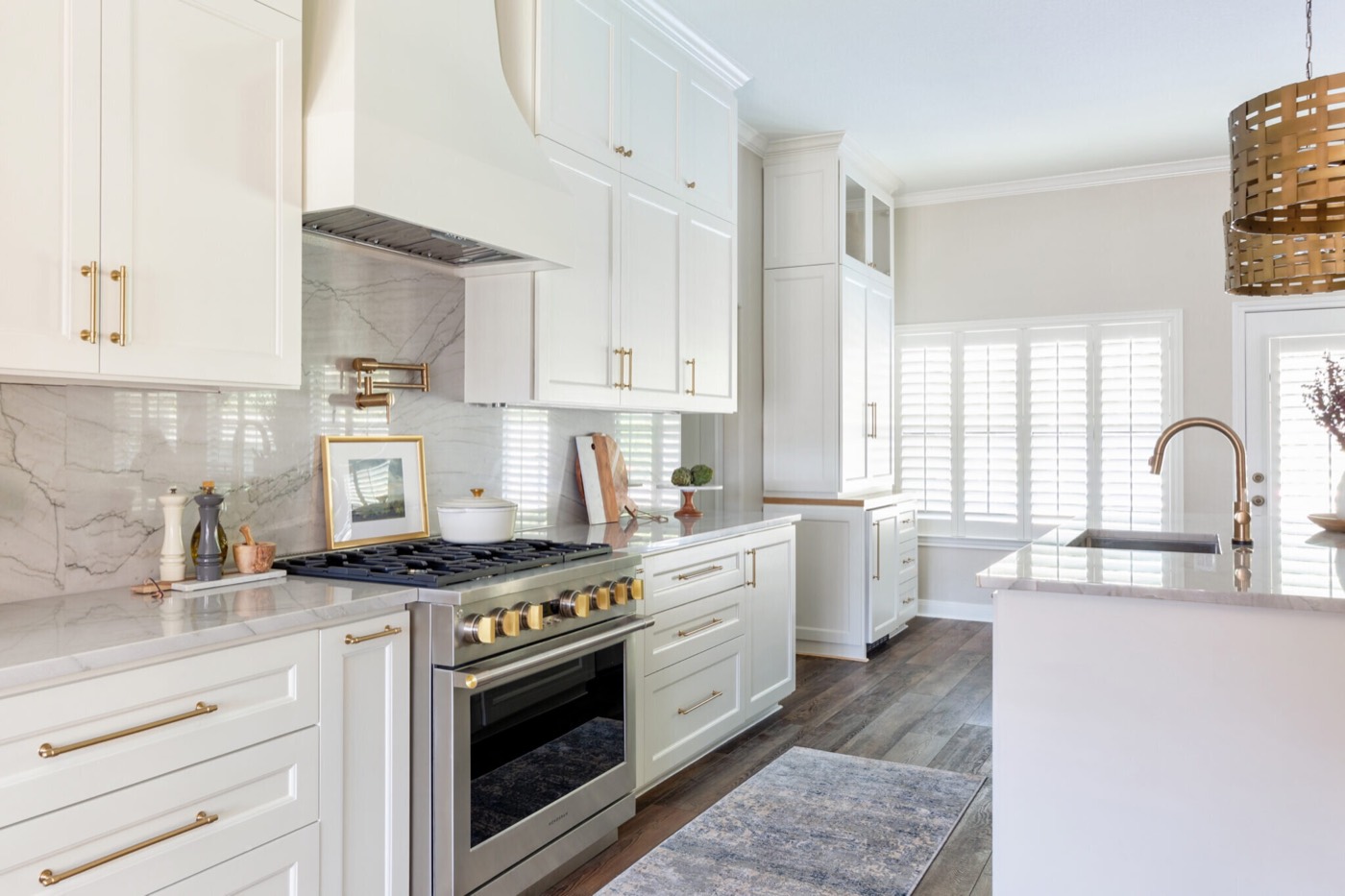 Kitchen range wall of white inset cabinetry and bookmatched marble slab opening to a shuttered garden door in the Knoll Kitchen project by Jennifer Kizzee Design
