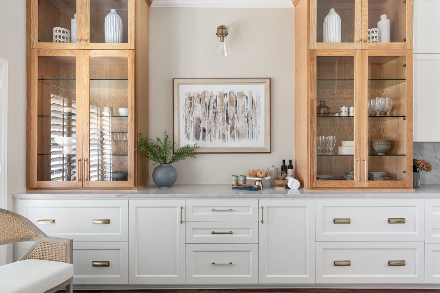 Serving buffet flanked by white oak glass front cabinets with a brass sconce above framed abstract art in the Knoll Kitchen project by Jennifer Kizzee Design