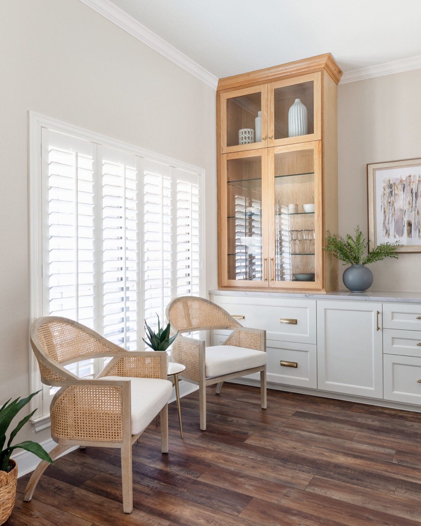 Corner sitting nook with two cane barrel chairs and a white oak glass front hutch beside plantation shutters in the Knoll Kitchen project by Jennifer Kizzee Design