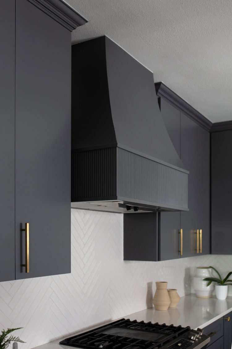 Fluted charcoal hood above the range with white herringbone tile in the Longwood project by Jennifer Kizzee Design