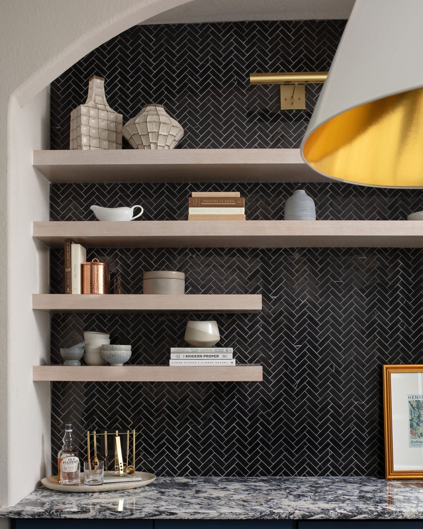 Arched bar niche lined in black herringbone tile with pale oak floating shelves in the Markee Oaks project by Jennifer Kizzee Design