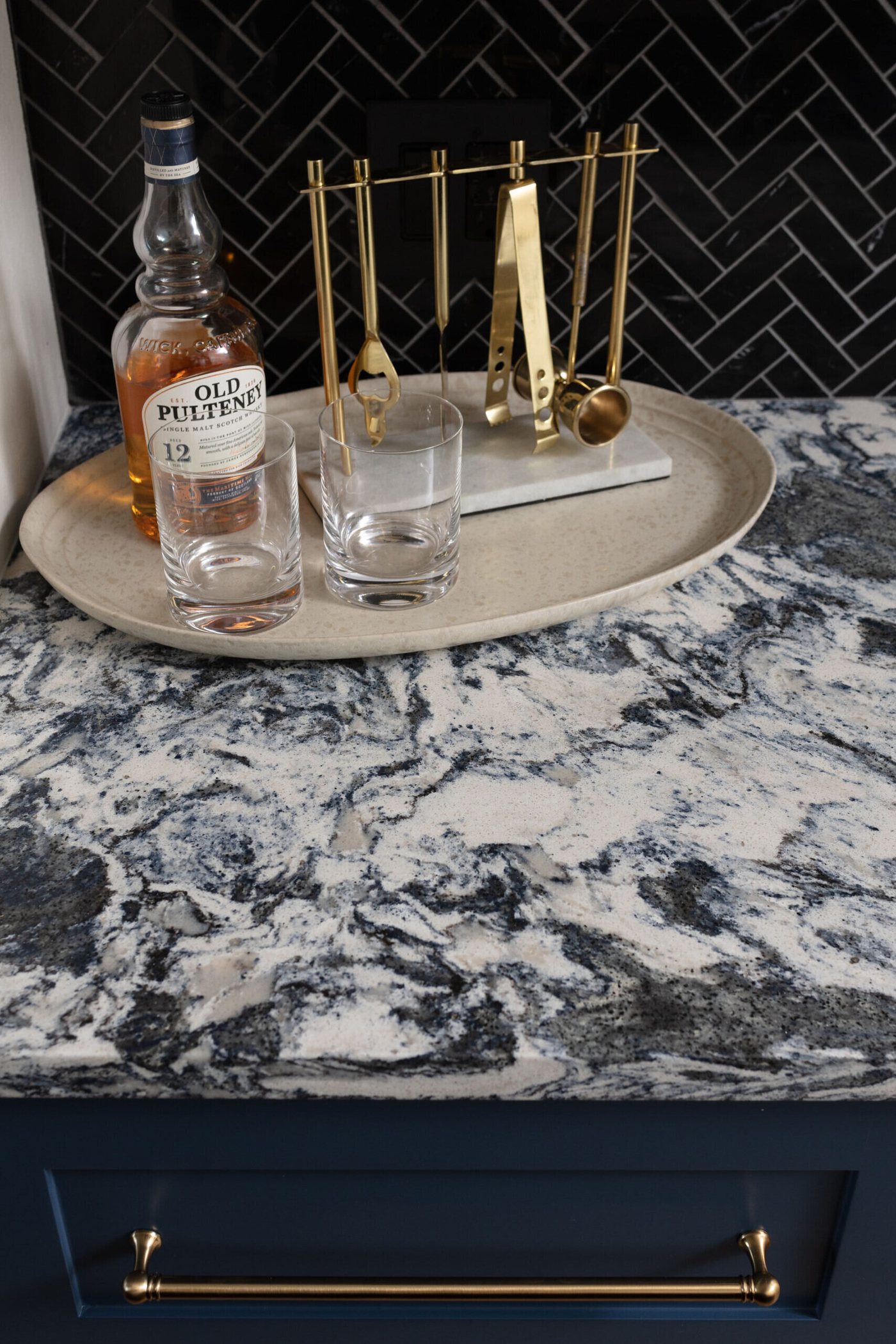 Blue and white granite bar counter with a brass tray and glassware in the Markee Oaks project by Jennifer Kizzee Design