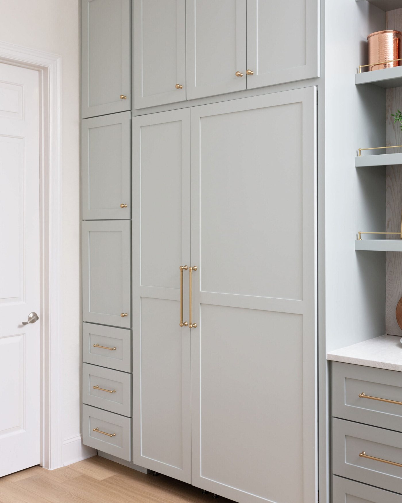 Floor to ceiling greige cabinetry with brass pulls beside the refrigerator in the Markee Oaks project by Jennifer Kizzee Design