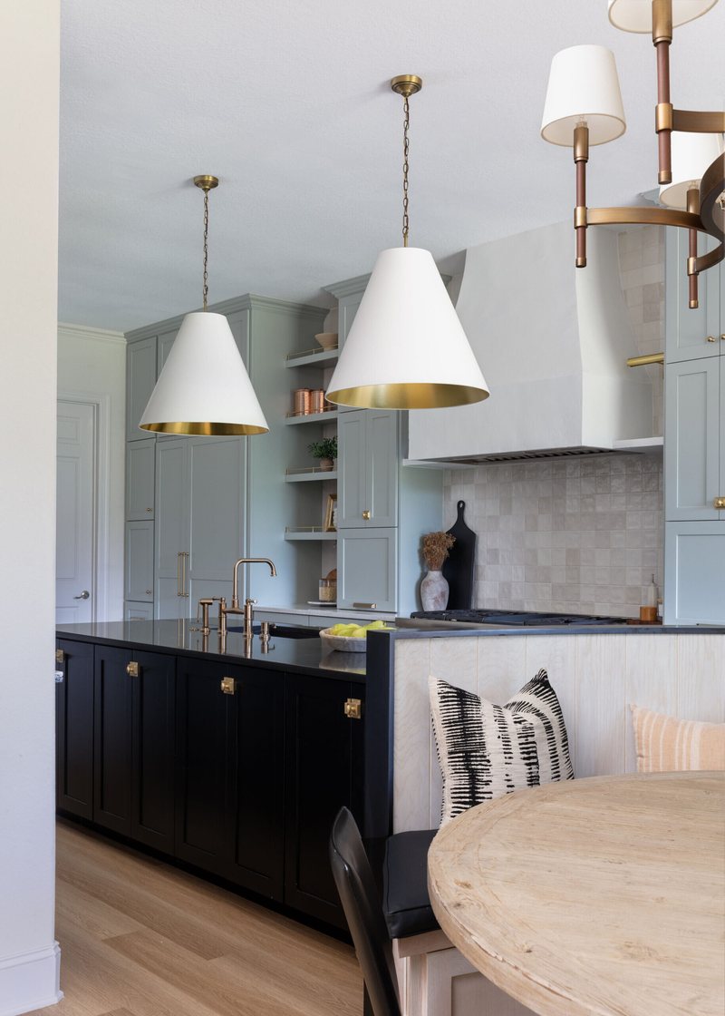 Navy kitchen with a black granite island, white cone pendants and a round dining table in the Markee Oaks project by Jennifer Kizzee Design