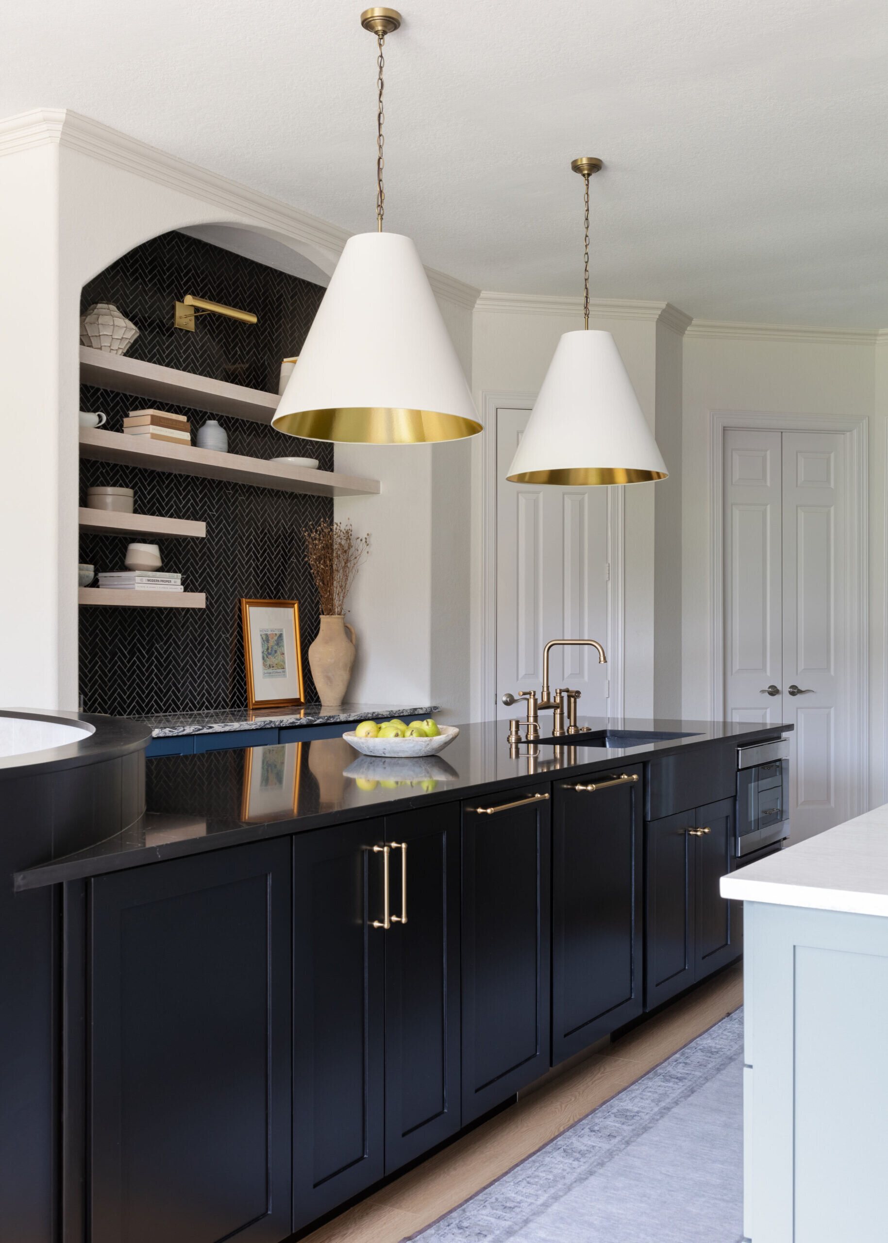 Navy kitchen island in black granite under white cone pendants lined in gold in the Markee Oaks project by Jennifer Kizzee Design